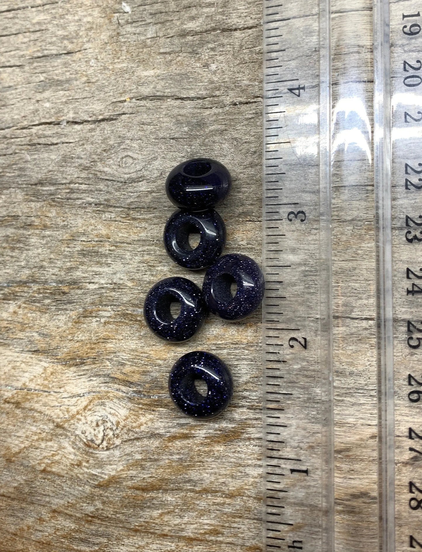 blue goldstone beads, each measuring 5mm in diameter. The beads exhibit a deep blue color with sparkling metallic flecks, creating a captivating and shimmering appearance next to a ruler