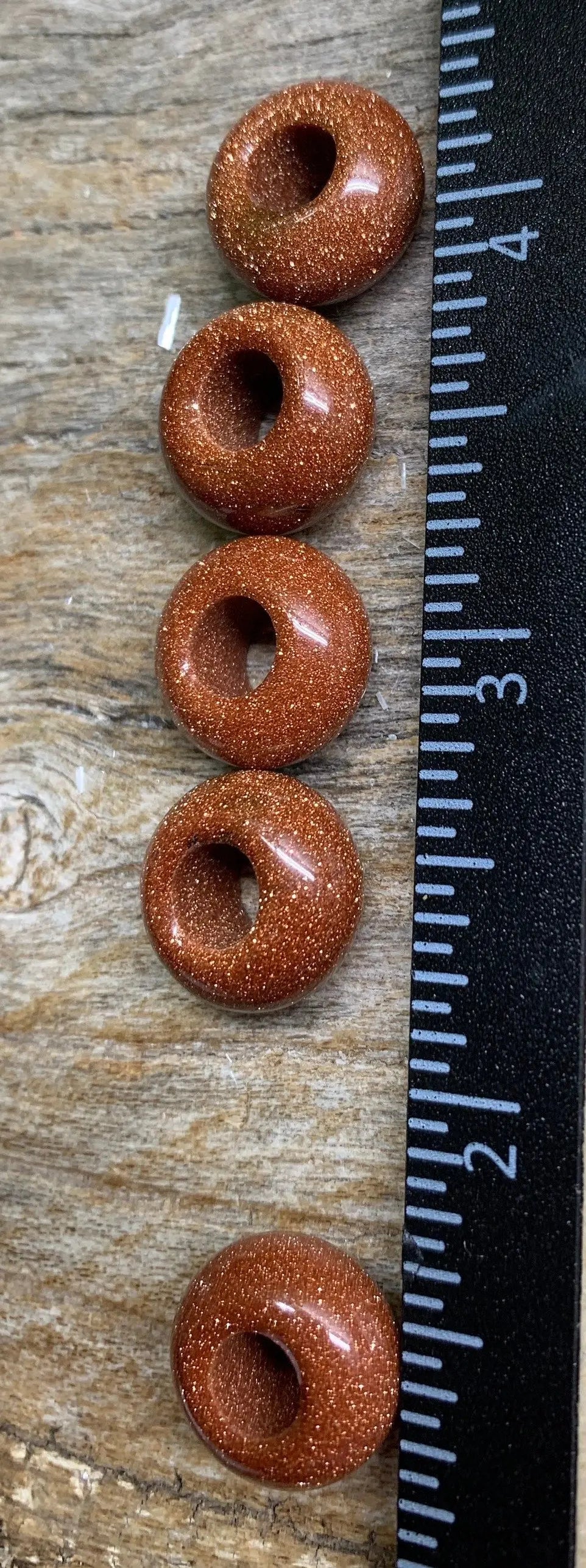 "Close-up view of 14mm goldstone beads, featuring sparkling coppery flecks against a dark background positioned next to a ruler