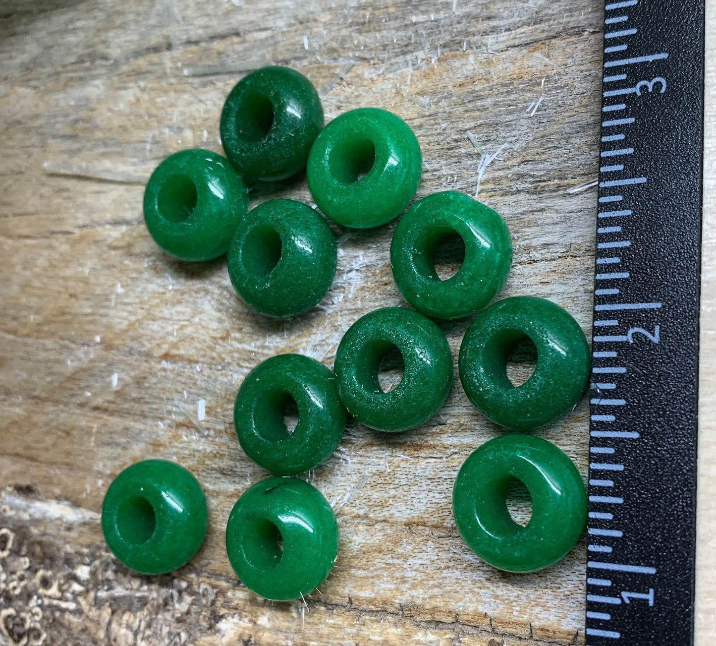vibrant green Quartz crystal 5mm beads, reflecting light and displaying natural variations in hue and texture mext to a ruler to show size