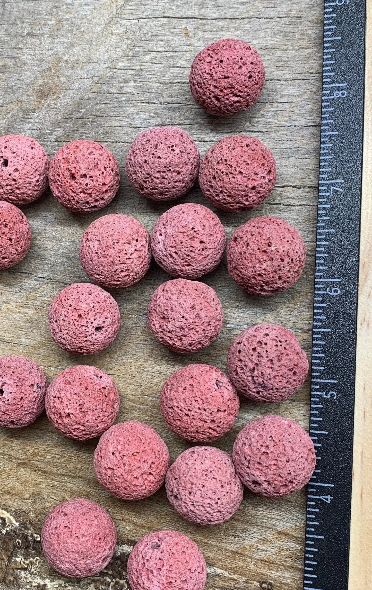 vibrant pink lava beads, formed through volcanic processes, showcasing a unique porous texture, next to a ruler