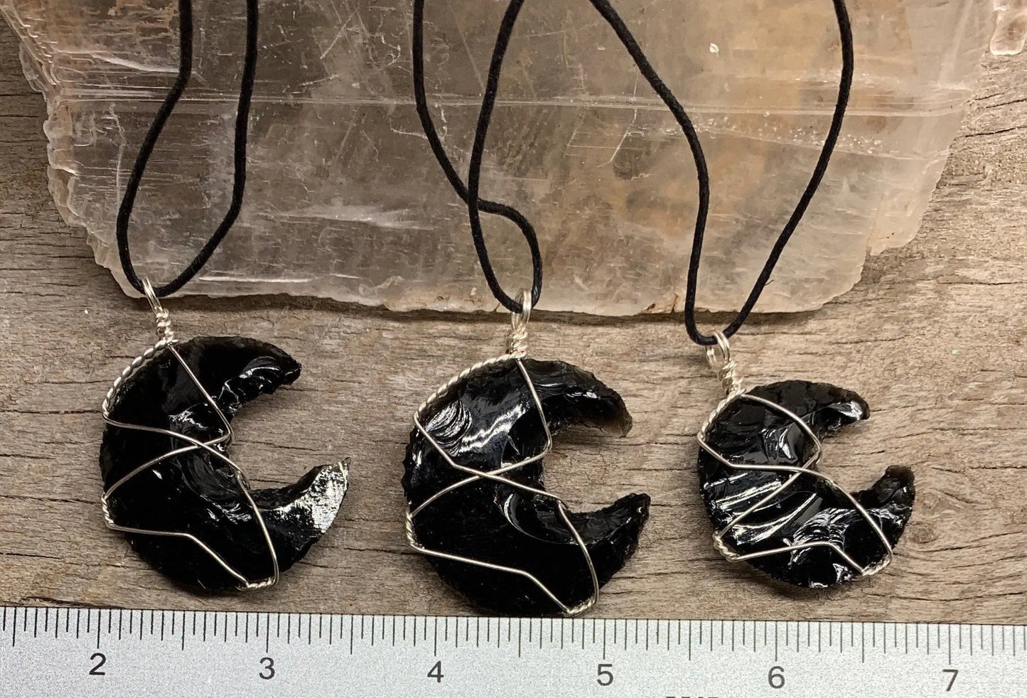 3 Silver wire wrapped obsidian crystal crescent moon pendants with adjustable black cords, displayed next to a ruler.