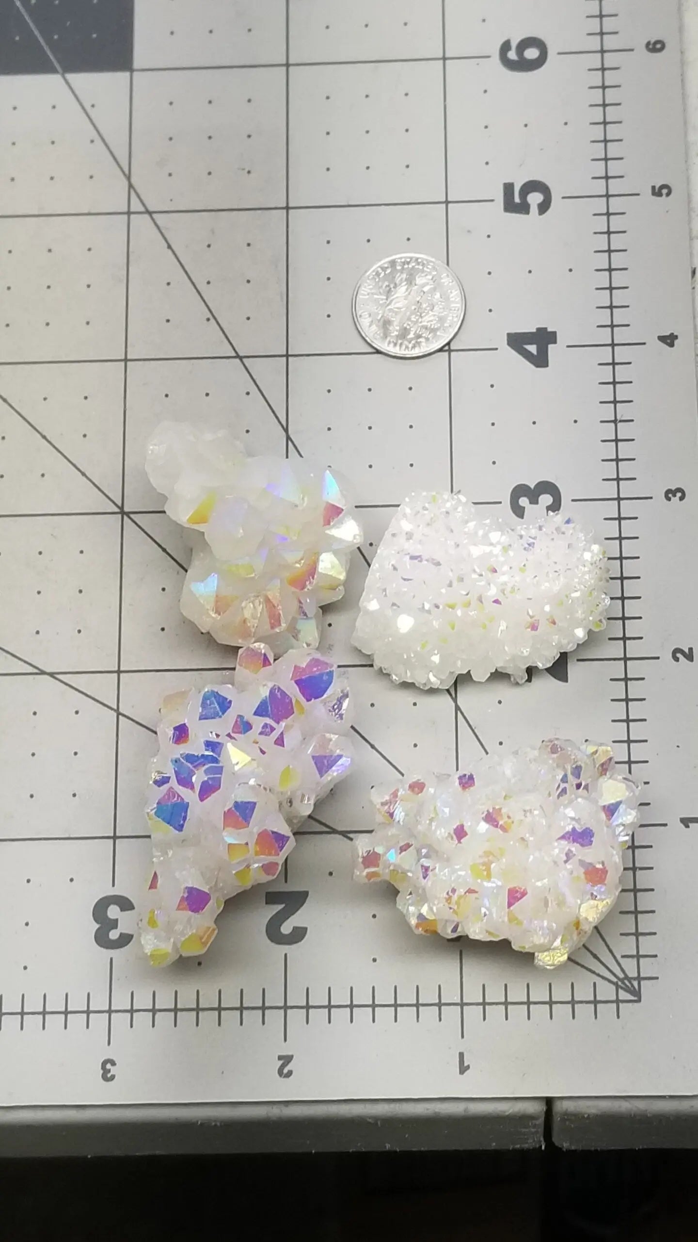 4 mesmerizing Angel Aura Quartz clusters featuring iridescent pastel hues, reflecting shades of pink, purple, and blue, with delicate crystal formations, displayed next to a ruler. Each quartz crystal is approximately 1 1/2” # 2”.