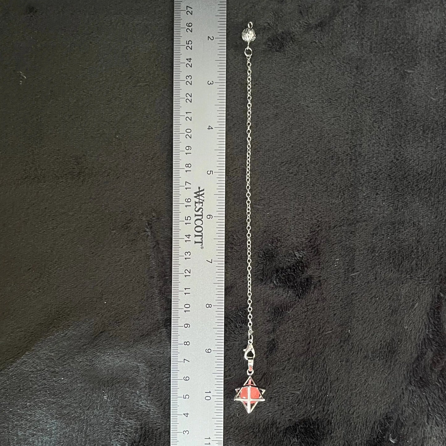 close up of a 1 cm cherry quartz sphere in a 1/2 inch sliver merkaba attatched to a 9 inch silver chain displayed next to a ruler