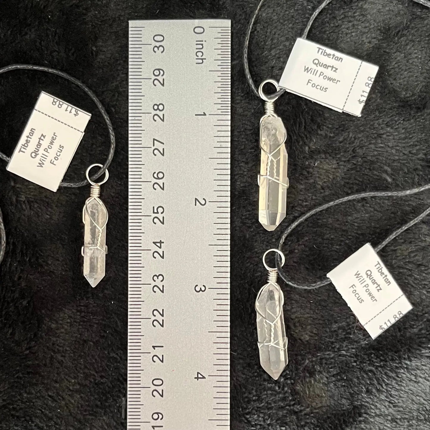 3 handmade ornately silver wire wrapped tibetan quartz crystal pendants, attatched to adjistable black cords, displayed next to a ruler to show size. The quartz crystals are approximately 1" - 1 1/4" in length.