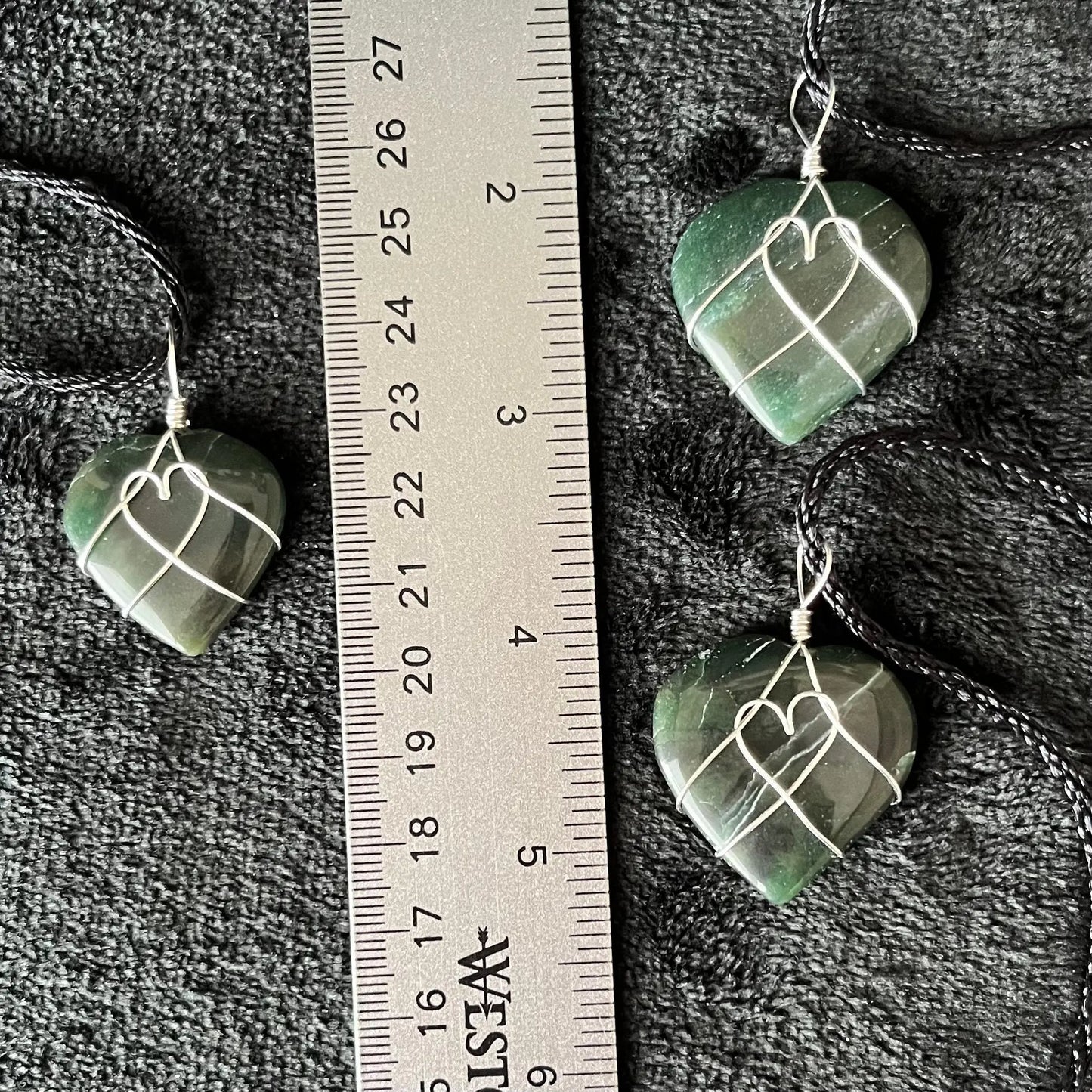 Silver wire wrapped, green jade heart pendants, approximately 3/4" X 1", attarched to adjustable black cords, displayed next to. ruler