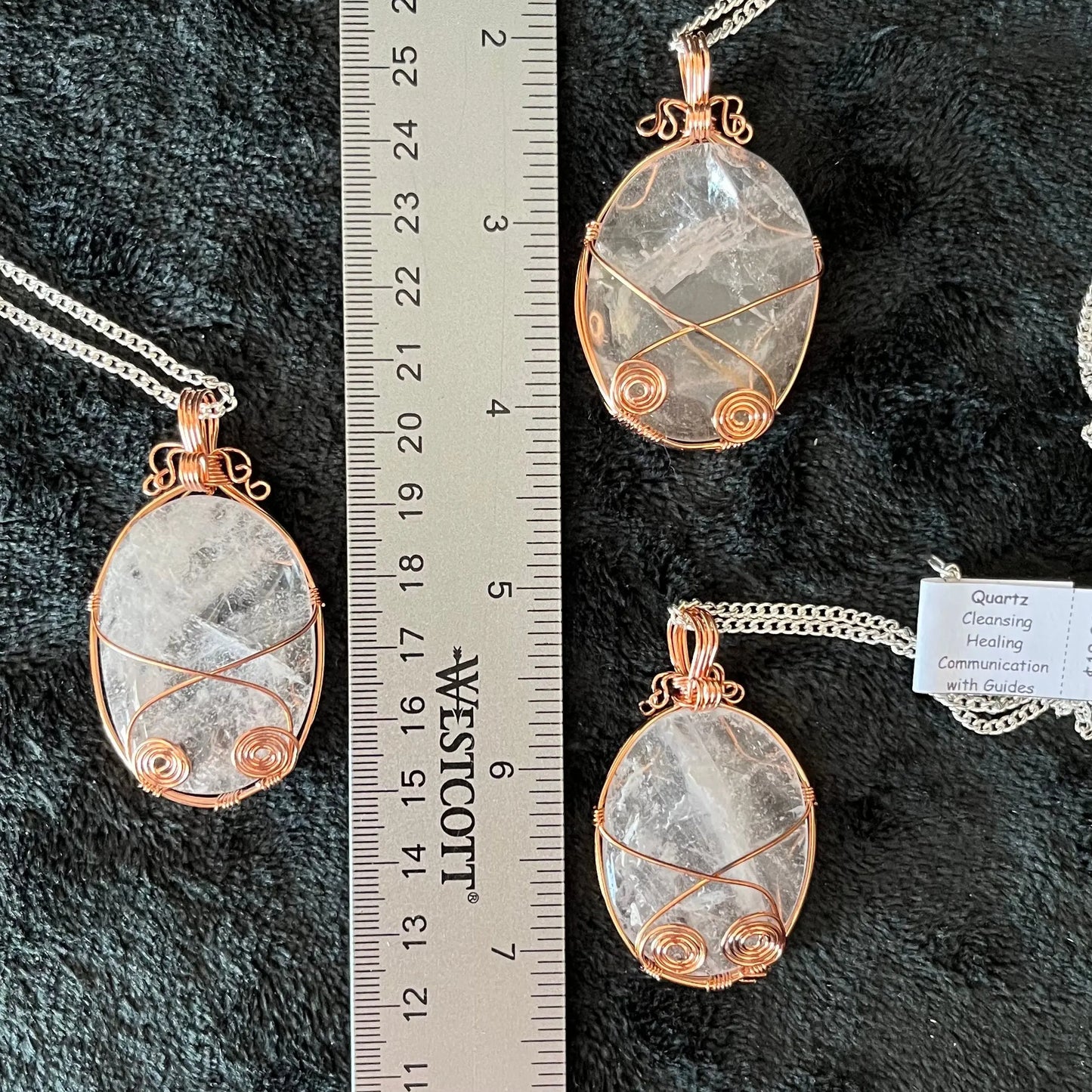 Three copper fancy wire wrapped clear quartz oval stone pendants attatched to a silver chains, displayed against a black background next to a ruler. eaxh oendant is 1 3/4" - 2 1/4" long