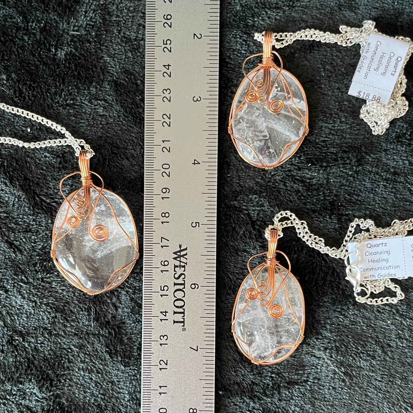Three fancy copper wire wrapped clear quartz oval stone pendants attatched to a silver chains, displayed against a black background next to a ruler. eaxh oendant is 1 3/4" - 2 1/4" long