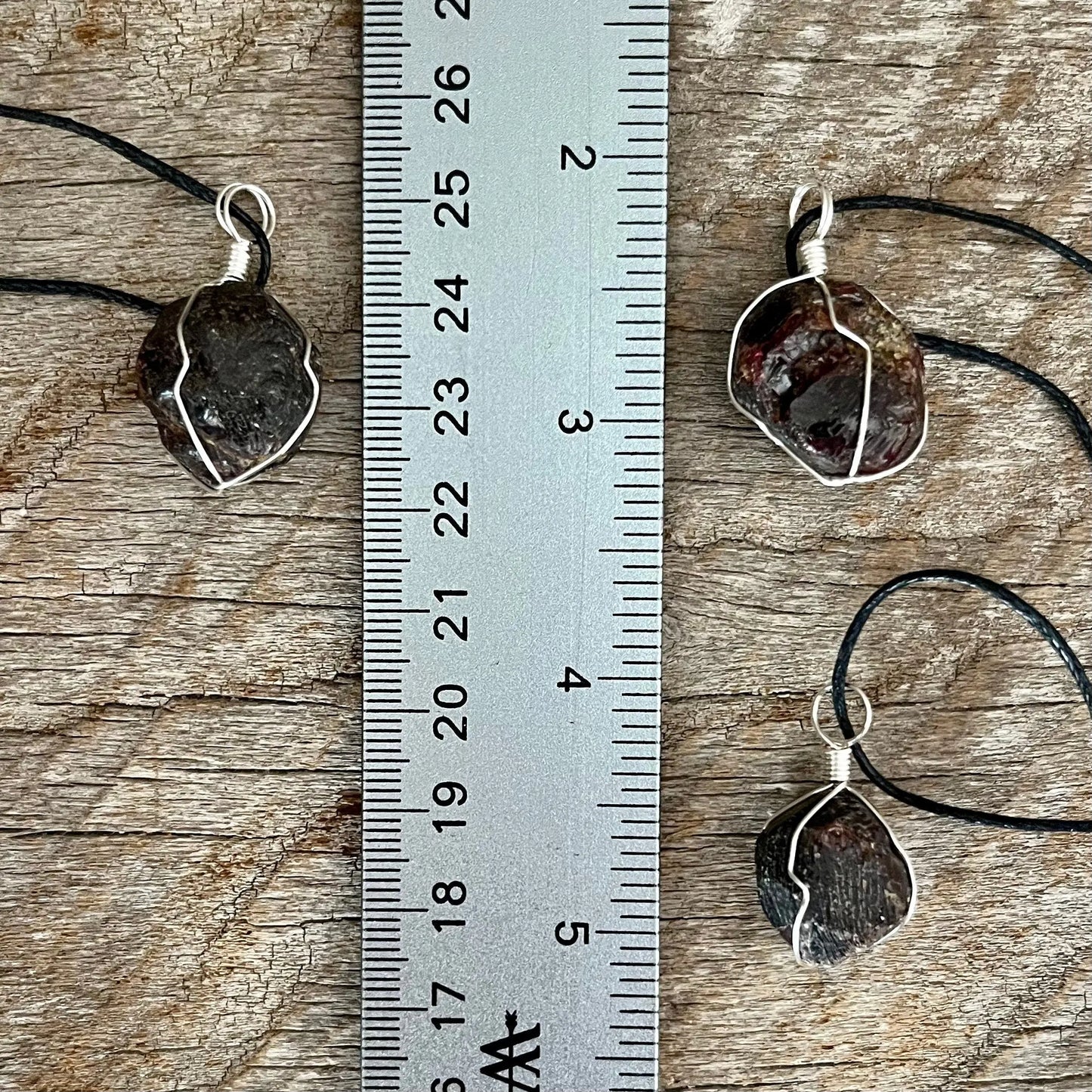 3 silver wire wrapped garnet crystal pendants attatched to adjistable black cords. displayed next to a ruler, pendant vary in diameter from 1/2" to 3/4"