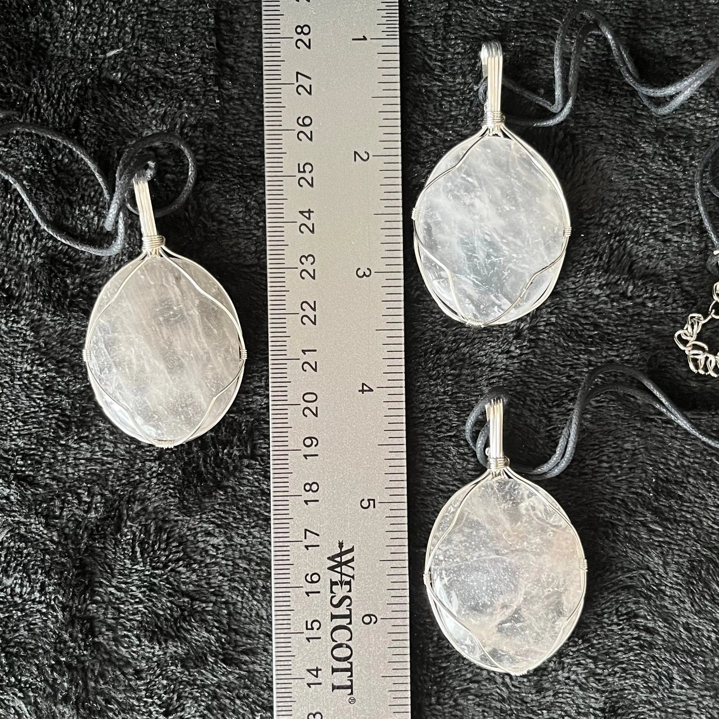 3 clear quartz worry stones beautifully silver wire wrapped in a way that frames the stone beautifully allowing access to the smoothe concave side on the back. pe dants are approximately 2 inches long and attatched to adjustable black cords, and displayed next to a ruler