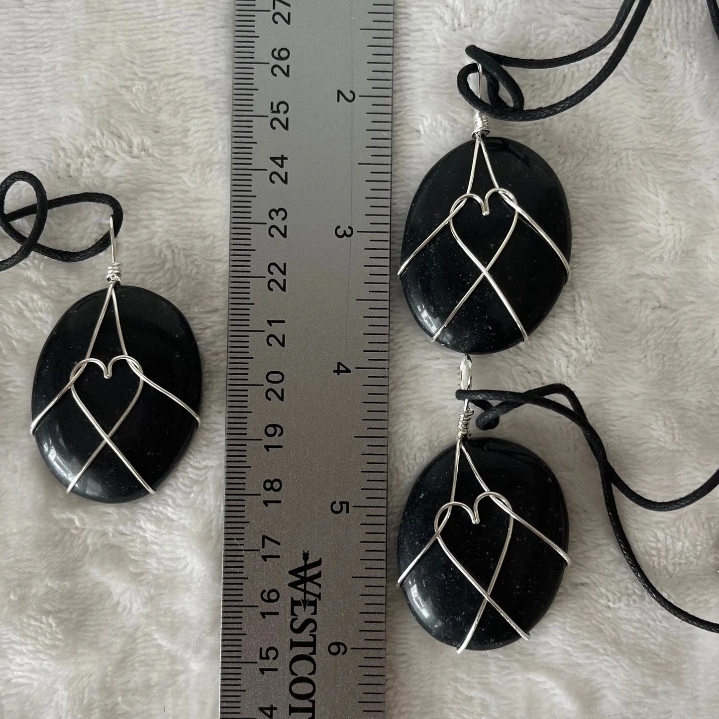 Silver wire wrapped obsidian worry stone pendants, with adjustable black cords. obsidian crystal are approximately 1 1/2" long. wire males a heart shape in the middle of the stones. Necklaces are displayed next to a ruler