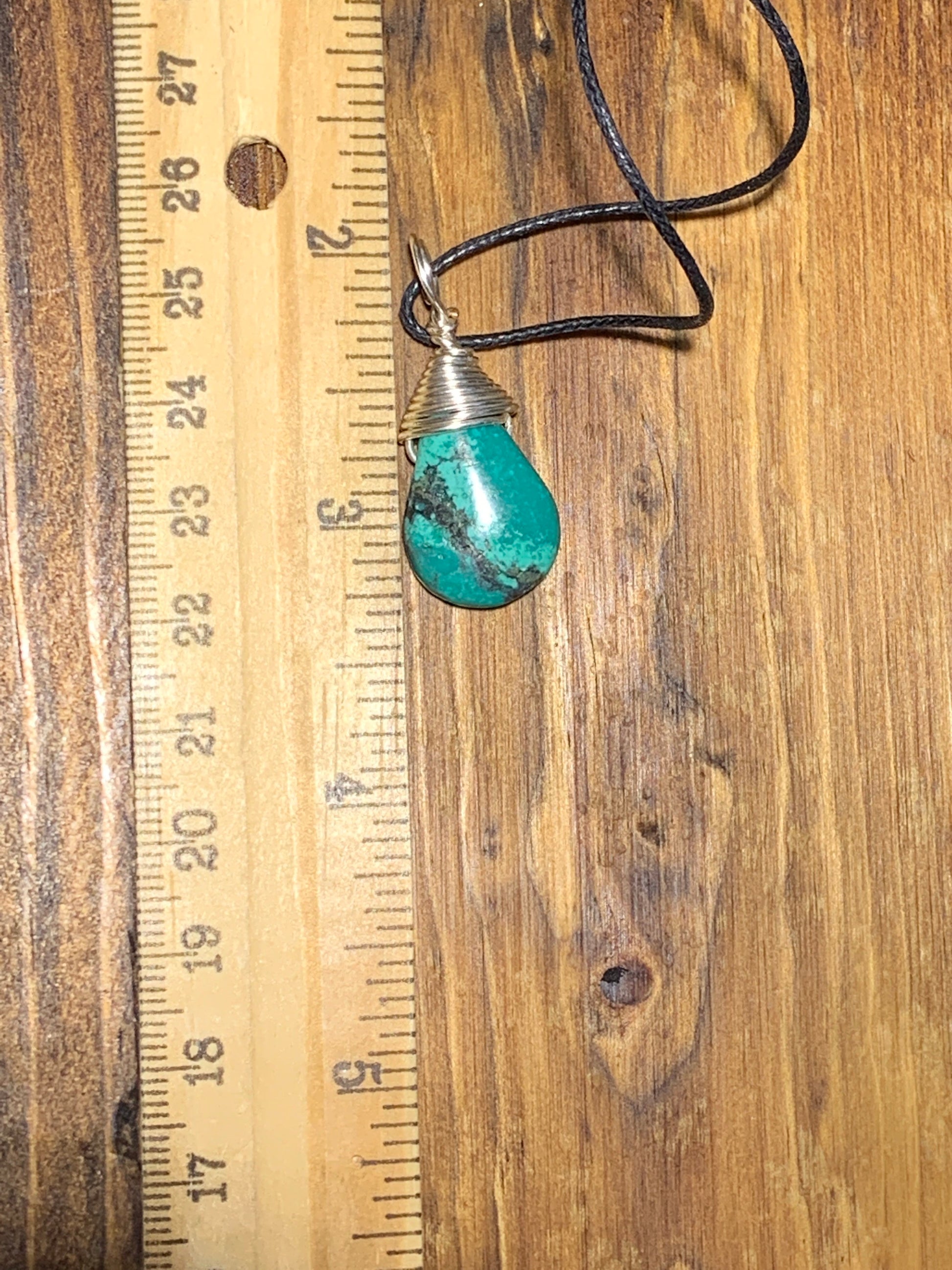 solver wire wrapped authentic turquoise cabochon tear drop pendant, approximately 1" long, attatched to an adjistable black cord, displayed next to a ruler