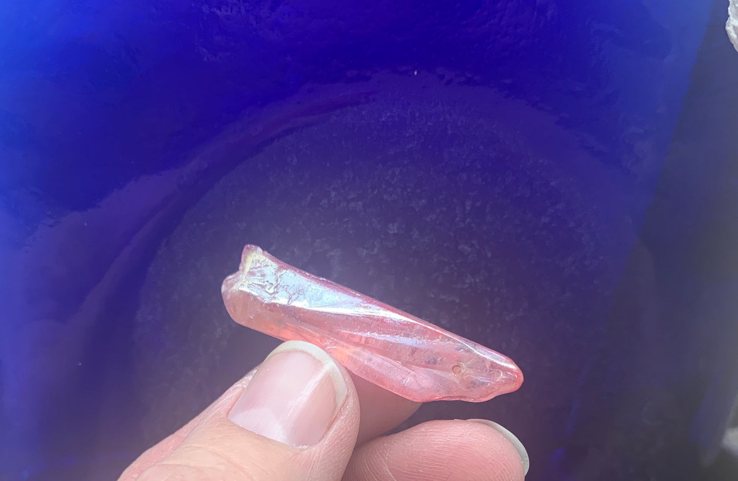 "Close-up of a delicate pink aura quartz bead being held by fingers, showcasing its ethereal beauty.