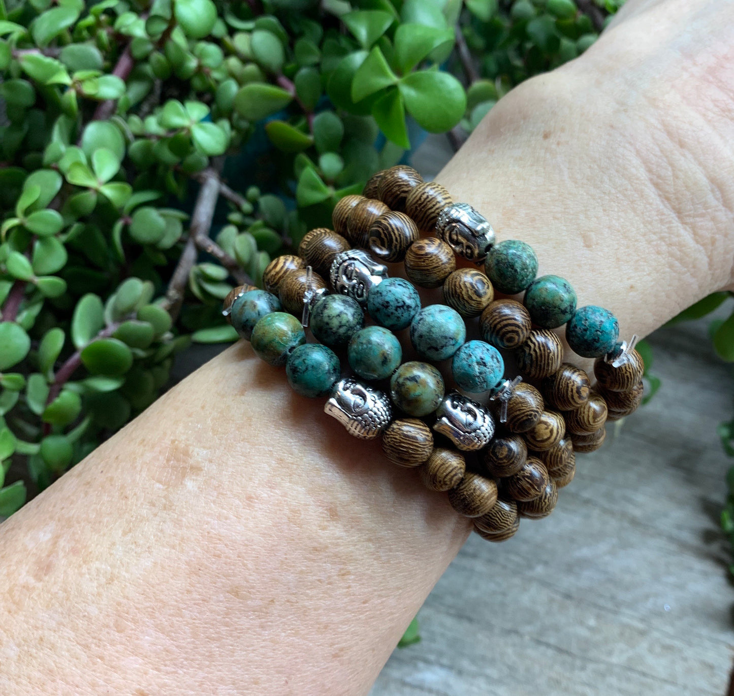 5 bracelets displayed on a forearm, each made of 8mm wooden beads, 3  african turquoise beads, and  1 budda head bead.