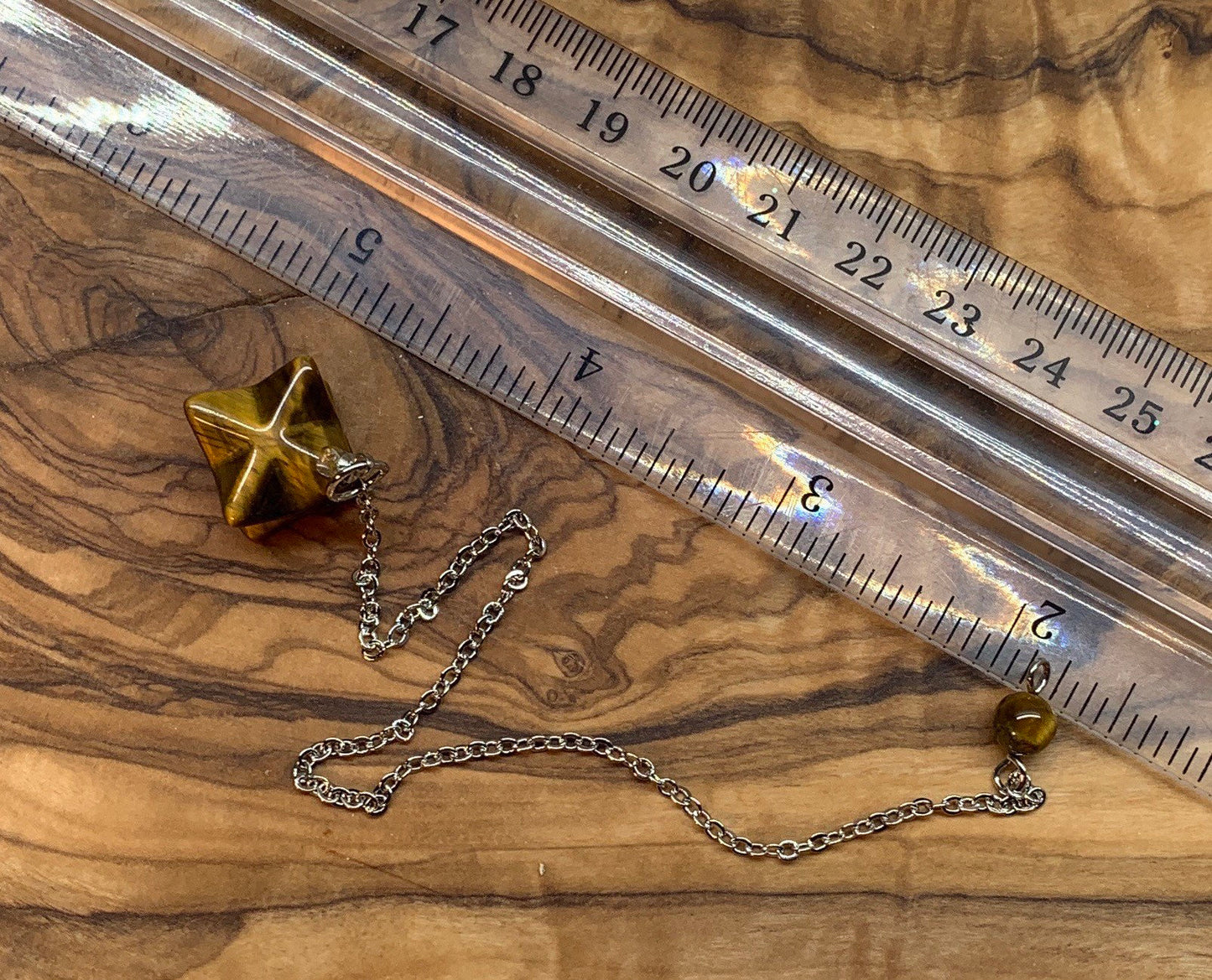 3/4" bronze and brown tiger eye merkaba shaped pendulum on an 8 inch silver chain next to a silver chain