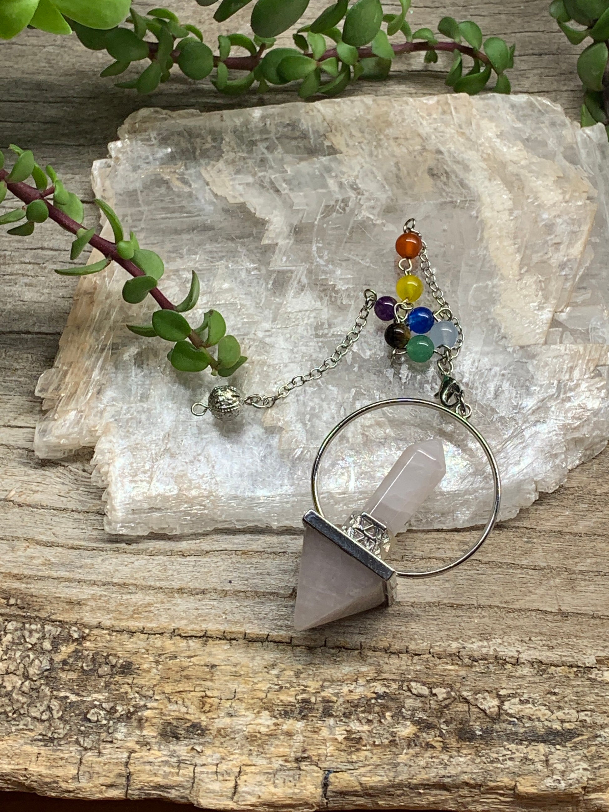 2 in pendulum including rose quartz inverted pyramid attached to rose quartz crystal point in a silver hoop, connected to an 8 inch chain including chakra beads. 