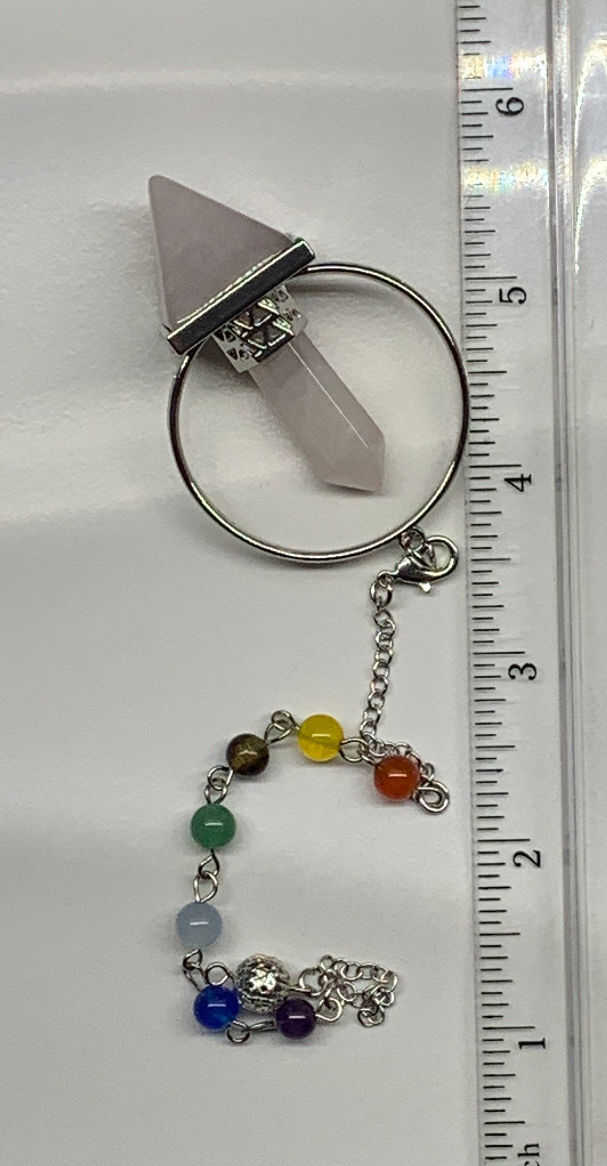 2 in pendulum including rose quartz inverted pyramid attached to rose quartz crystal point in a silver hoop, connected to an 8 inch chain including chakra beads next to a ruler against a white background