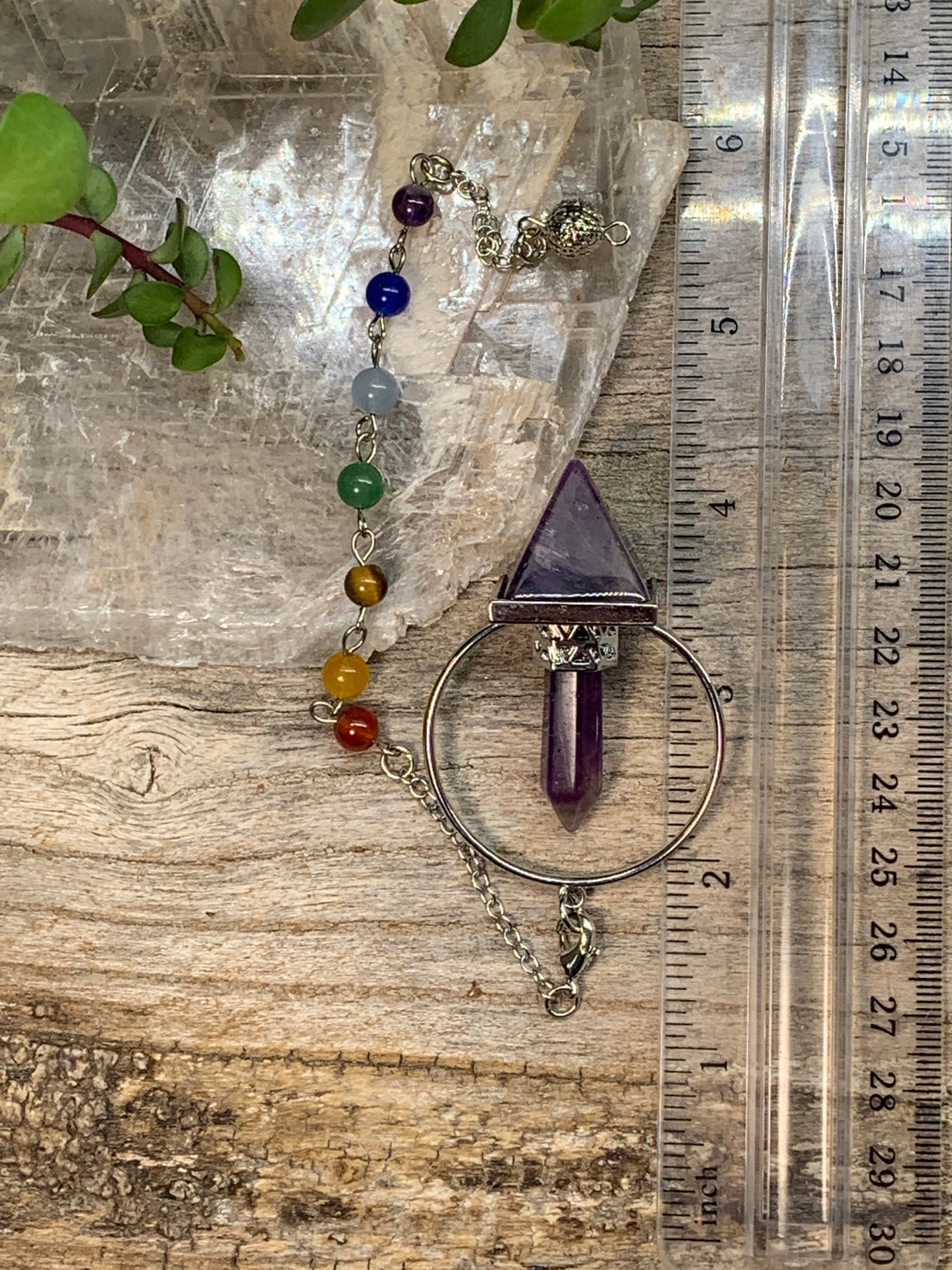 2 inch amethyst pendulum including an inverted amethyst pyramid attatched to an amethyst crystal in a silver ring, suspended from an 8 inch silver chain including chakra beads, displayed next to a ruler to show size