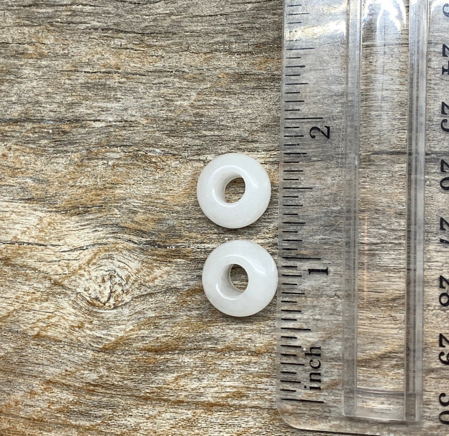 Close-up of 14mm snow quartz crystal beads, showcasing their translucent white color and smooth surface texture mext to a ruler