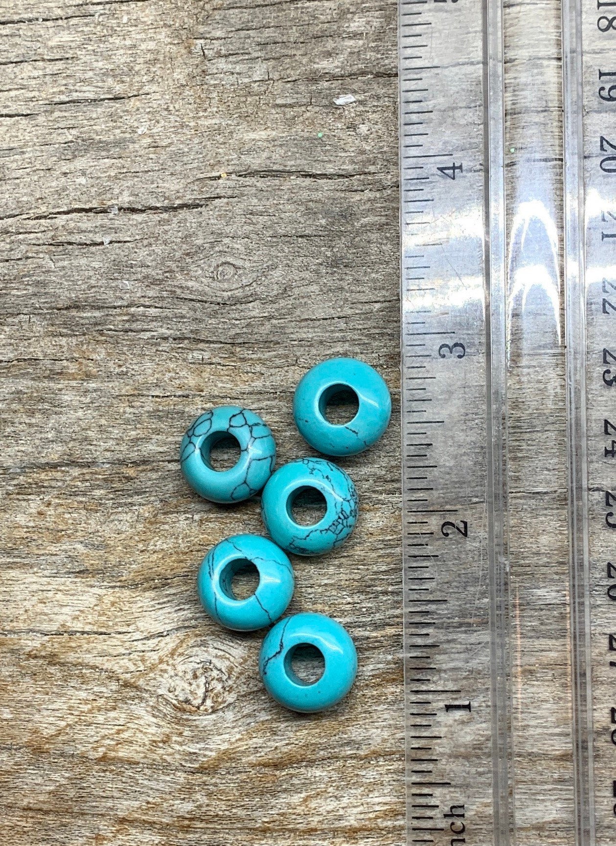 "Close-up of 14mm blue howlite crystal beads, showcasing their vibrant blue color and unique marbled patterns, next ro a ruler