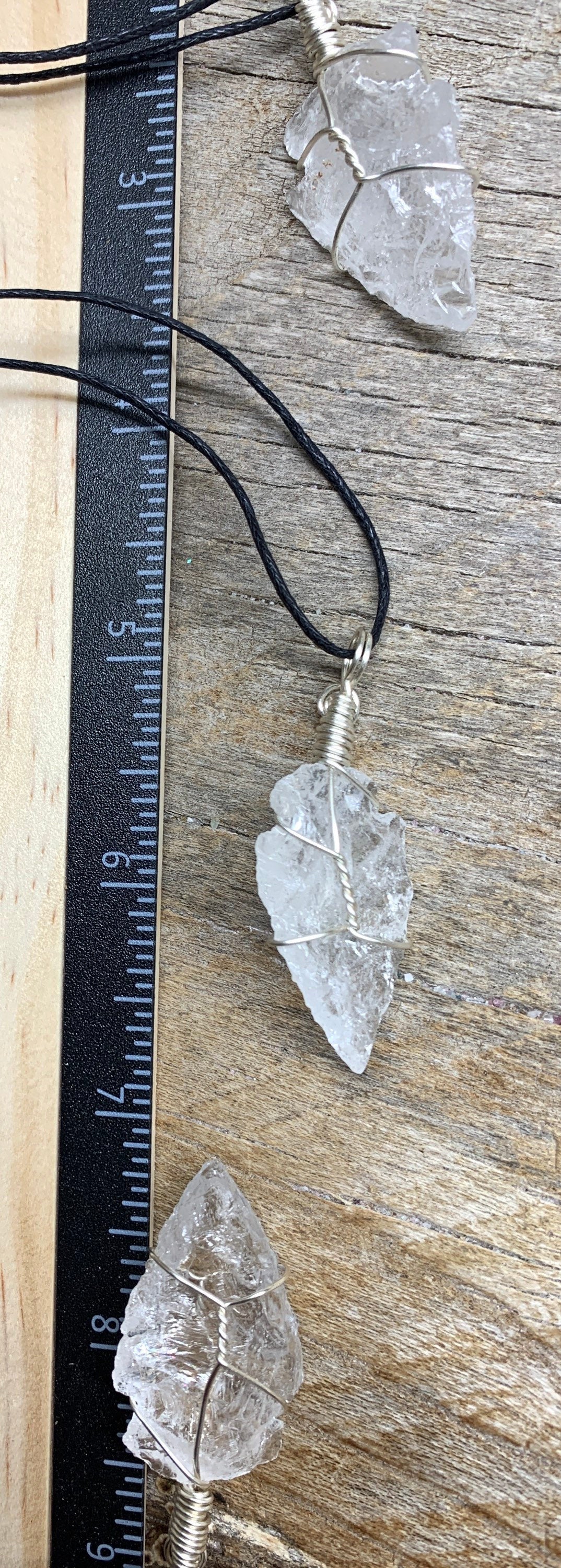 3 silver wire wrapped clear quartz pendants attetched to adjustable black cords, displayed next to a ruler.  arrowheads are 1 1/2" - 1 3/4" long 