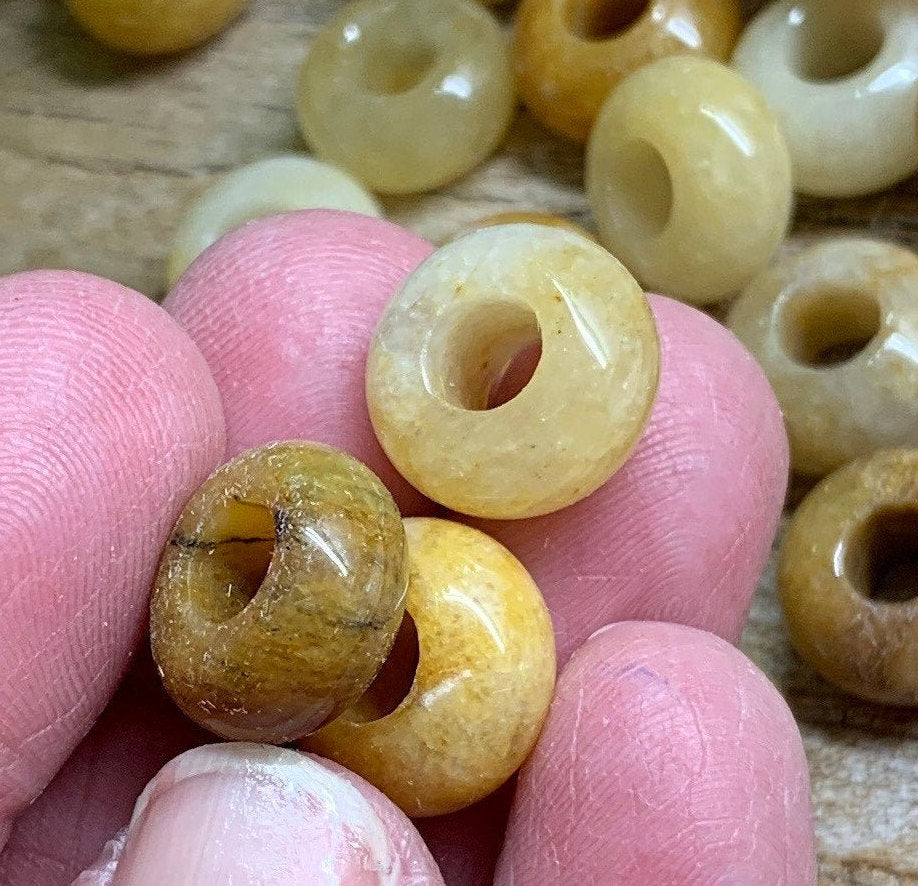 The yellow quartz beads in the close-up appear to have a vibrant, sunny yellow color with a smooth, polished surface. Each bead is approximately 5/8 inch in size, showcasing a translucent quality that allows light to pass through, creating a subtle glow. The hand holding the beads adds a human touch to the image, emphasizing their size and providing a sense of scale.