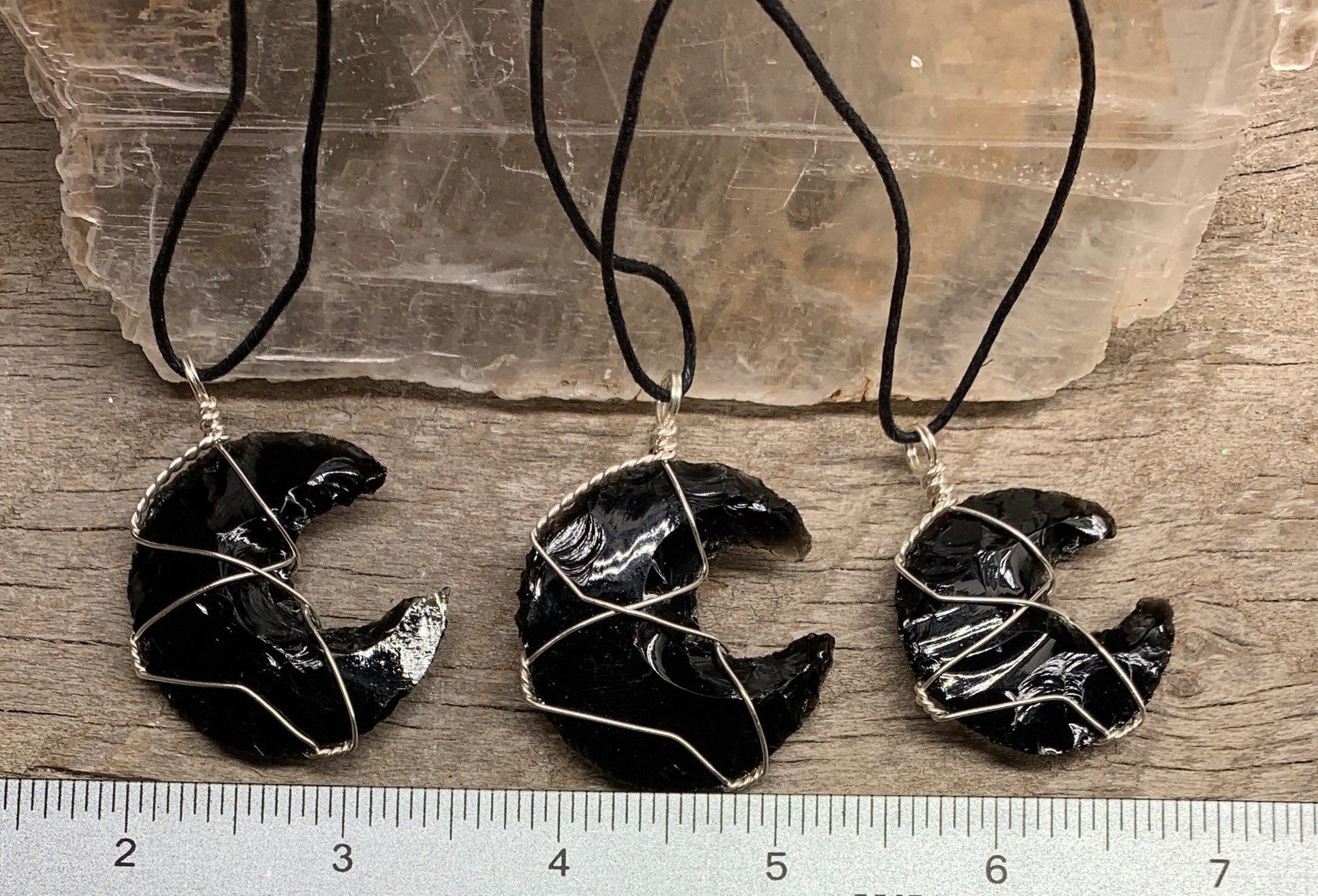 3 Silver wire wrapped obsidian crystal crescent moon pendants with adjustable black cords, displayed next to a ruler.