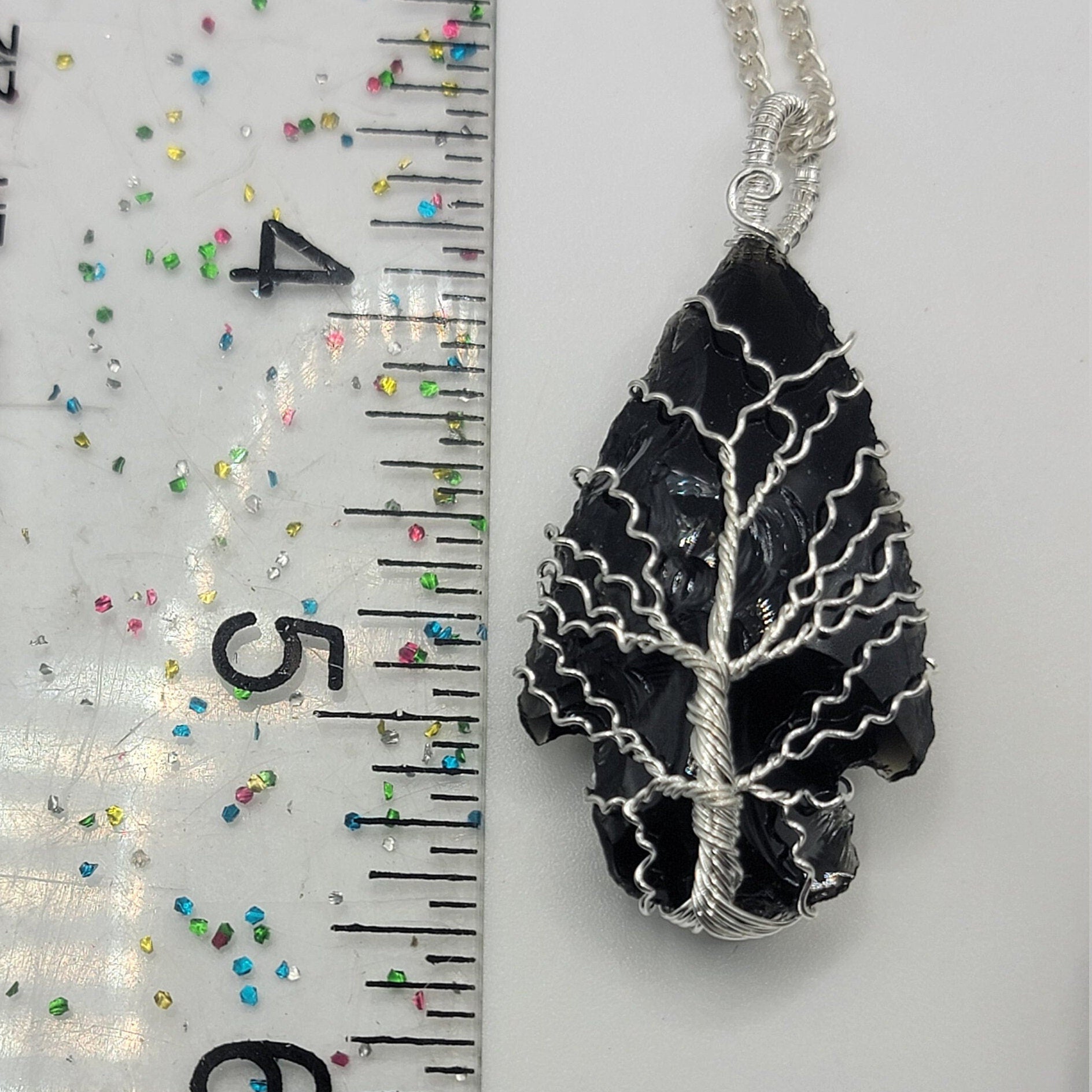 black obsidian 1 1/2" arrowhead, silver wire wrapped, handmade, pendant attarched to a silver chain, dosplayed next ro a ruler.