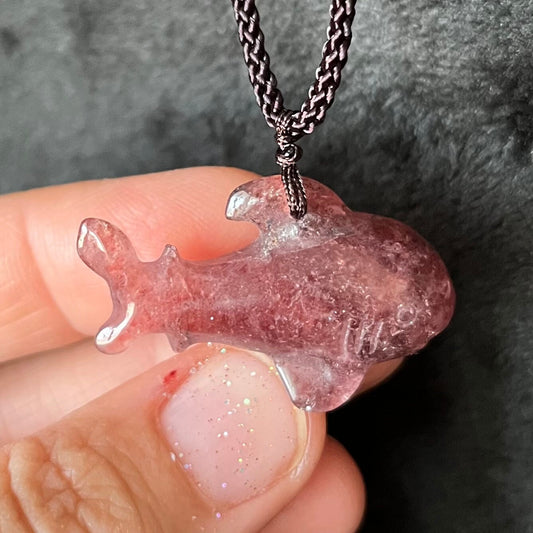 Close-up of a translucent, pink strawberry quartz, shark pendant suspended from adjustable brown cord