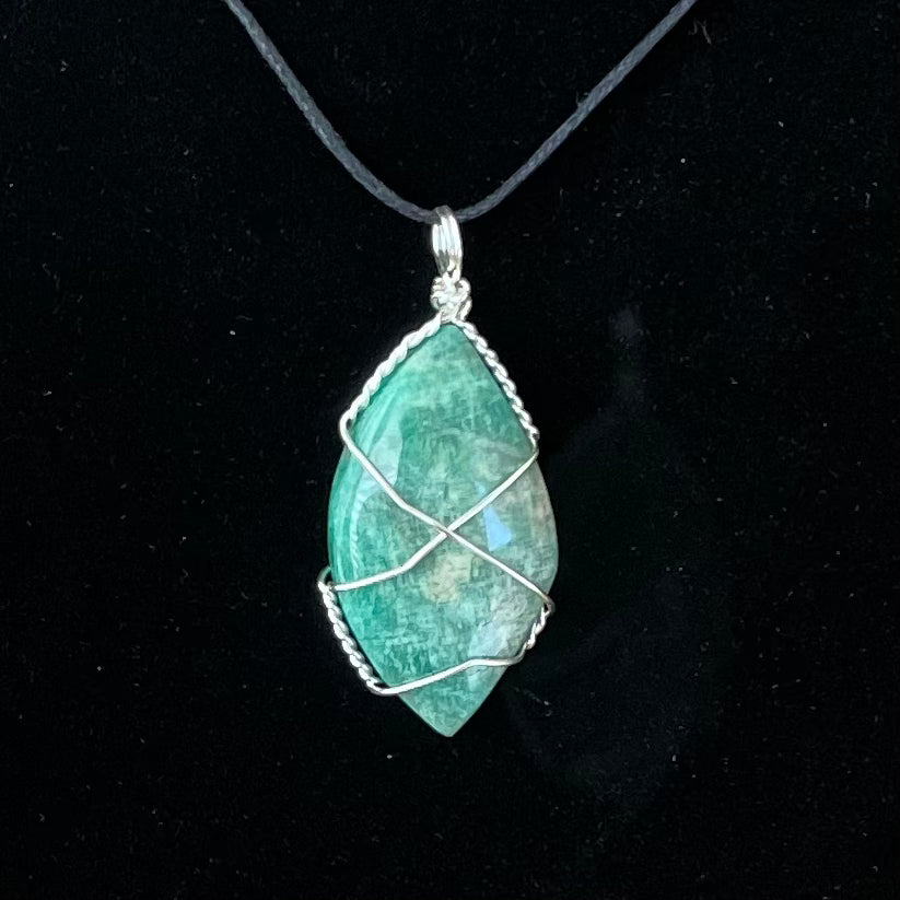 Amazonite football shaped cabochon silver wire wrapped pendant attached to an adjustable black cord displayed against a black background to enhance the vibrant blue, green color and mottled white patterns and streaks characteristic of the stone