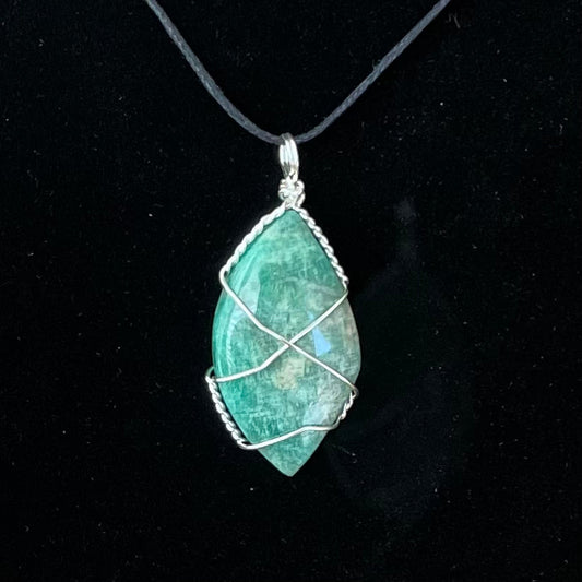 Amazonite football shaped cabochon silver wire wrapped pendant attached to an adjustable black cord displayed against a black background to enhance the vibrant blue, green color and mottled white patterns and streaks characteristic of the stone