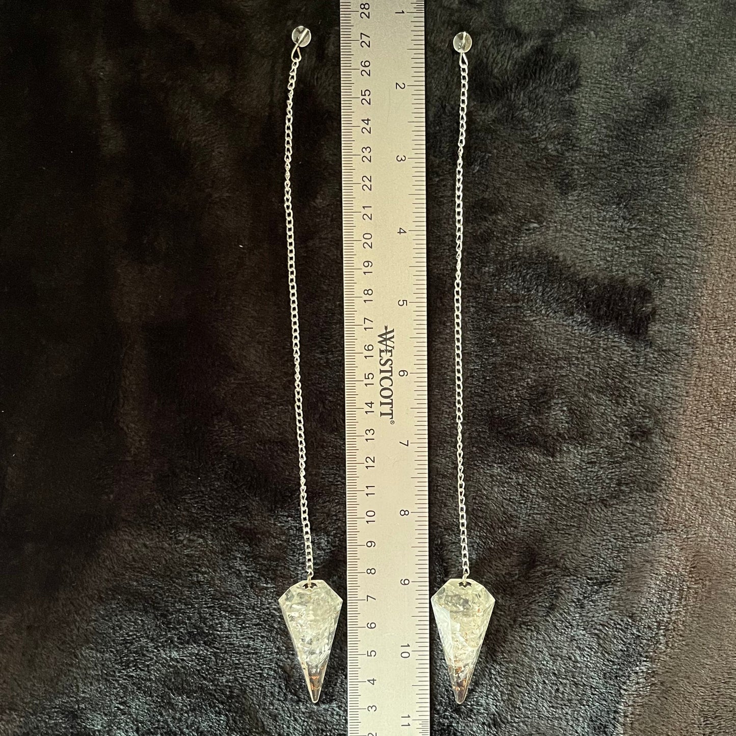 Two, 2 inch clear quartz crystal point orgonite pendulum attatched to silver 8 inch chains displayed next to a ruler to show size.