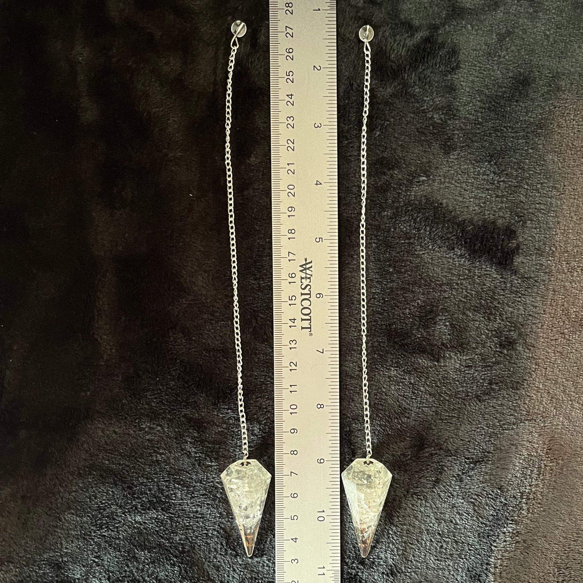 Two, 2 inch clear quartz crystal point orgonite pendulum attatched to silver 8 inch chains displayed next to a ruler to show size.