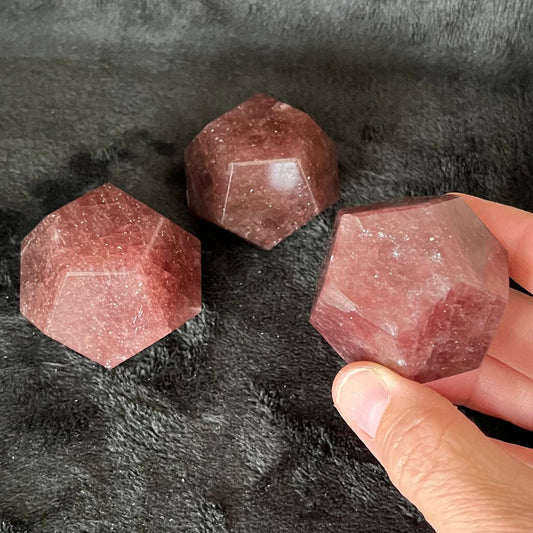 Three beautiful translucent, pink strawberry quartz dodecahedrons displayed against a black background.