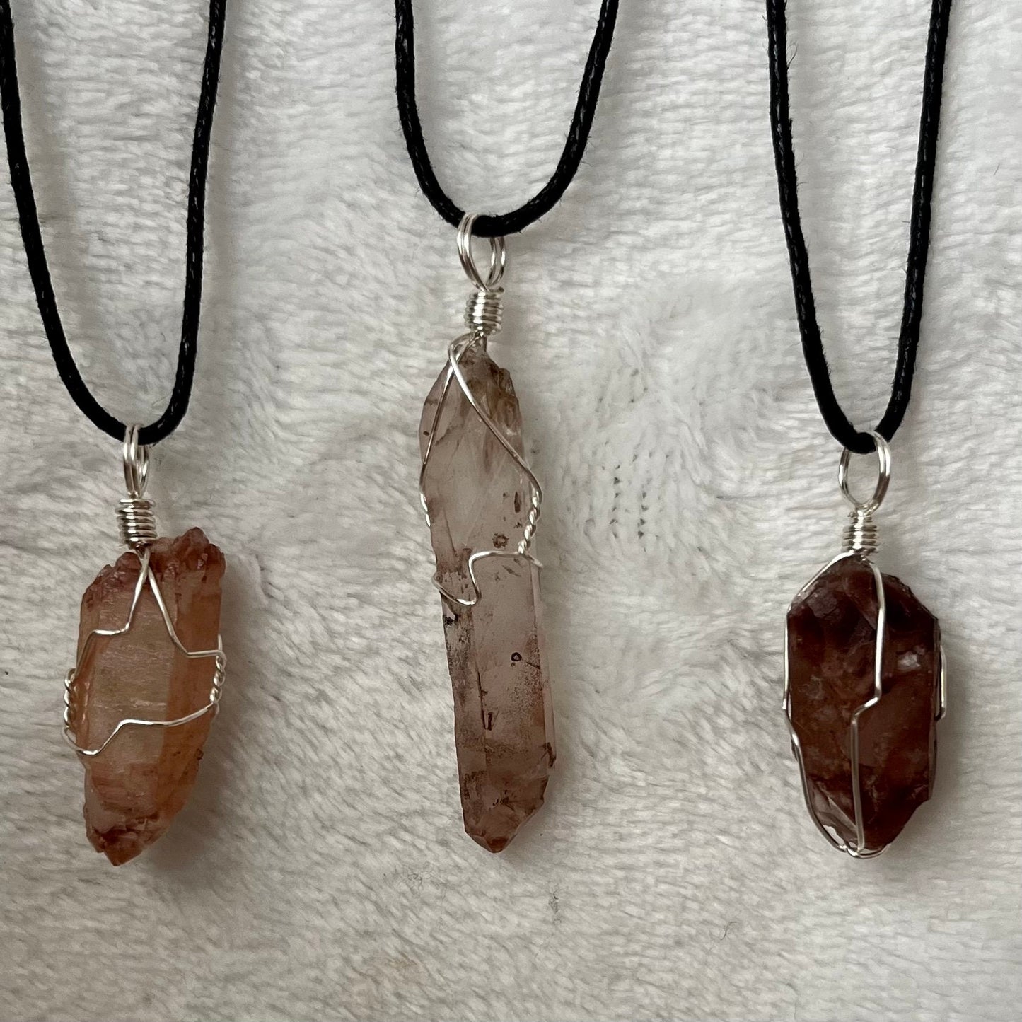 3 ornately silver wire wrapped lithium quartz pendants varying im color from clear to orange to red, including black cords displayed against a white background