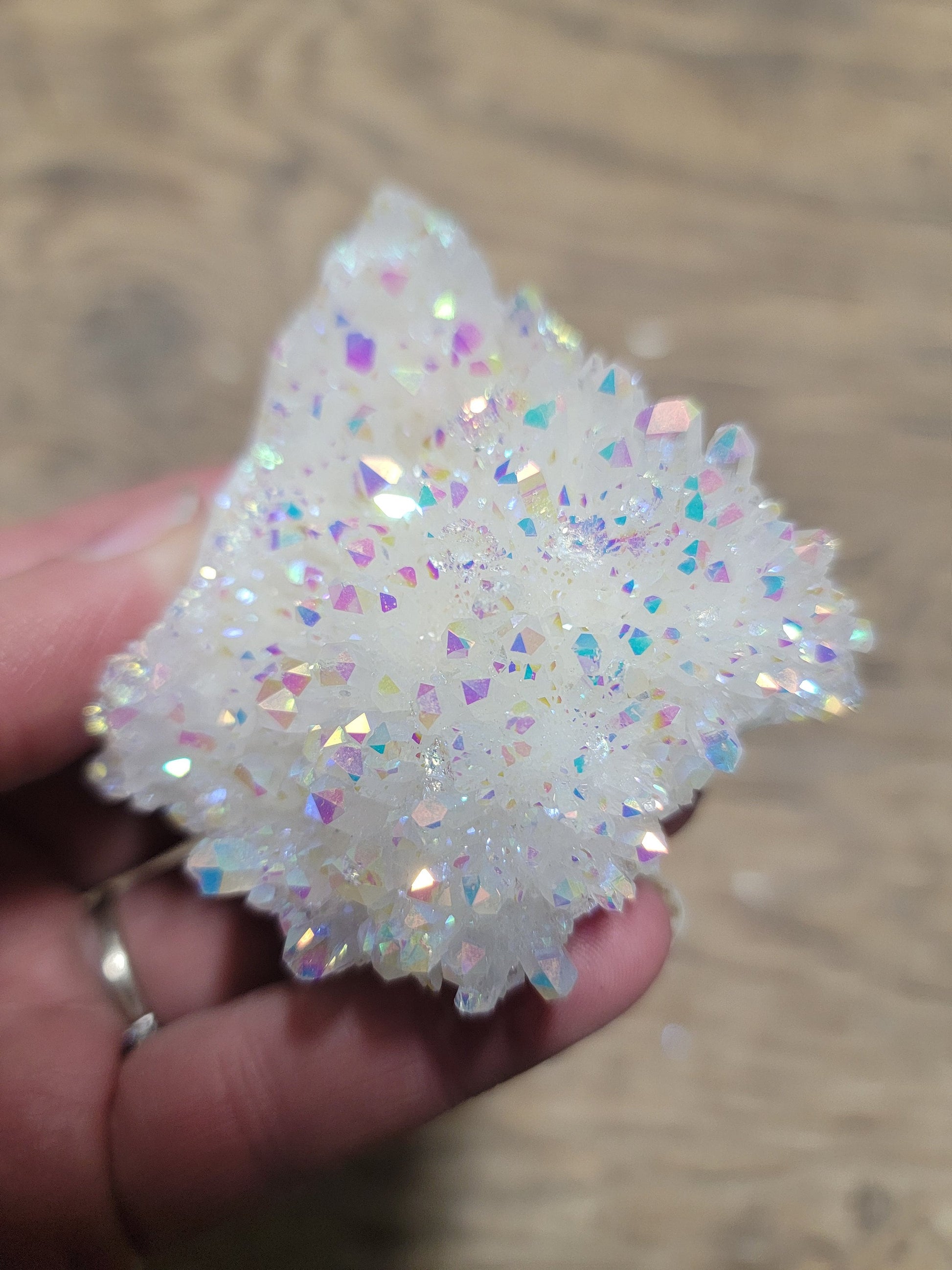 A mesmerizing Angel Aura Quartz cluster featuring iridescent pastel hues, reflecting shades of pink, purple, and blue, with delicate crystal formations that ."