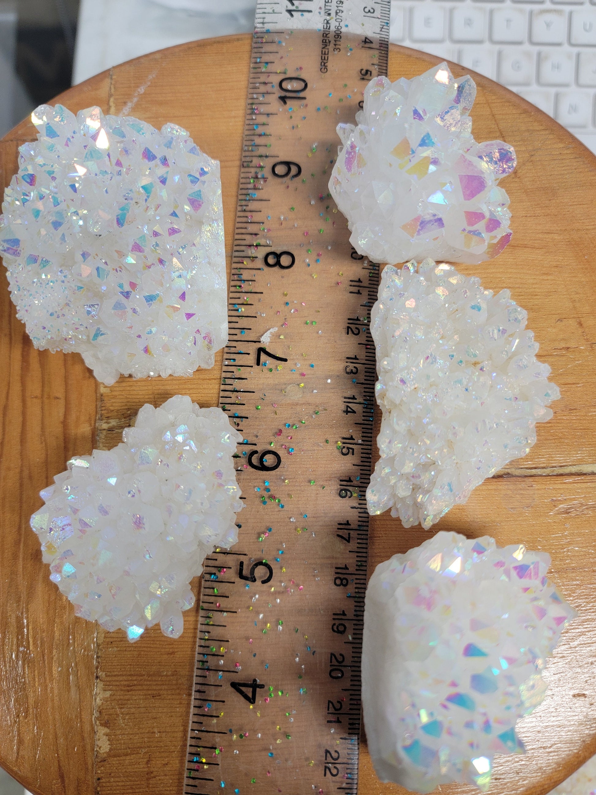 5 mesmerizing Angel Aura Quartz clusters featuring iridescent pastel hues, reflecting shades of pink, purple, and blue, with delicate crystal formations, displayed next to a ruler.