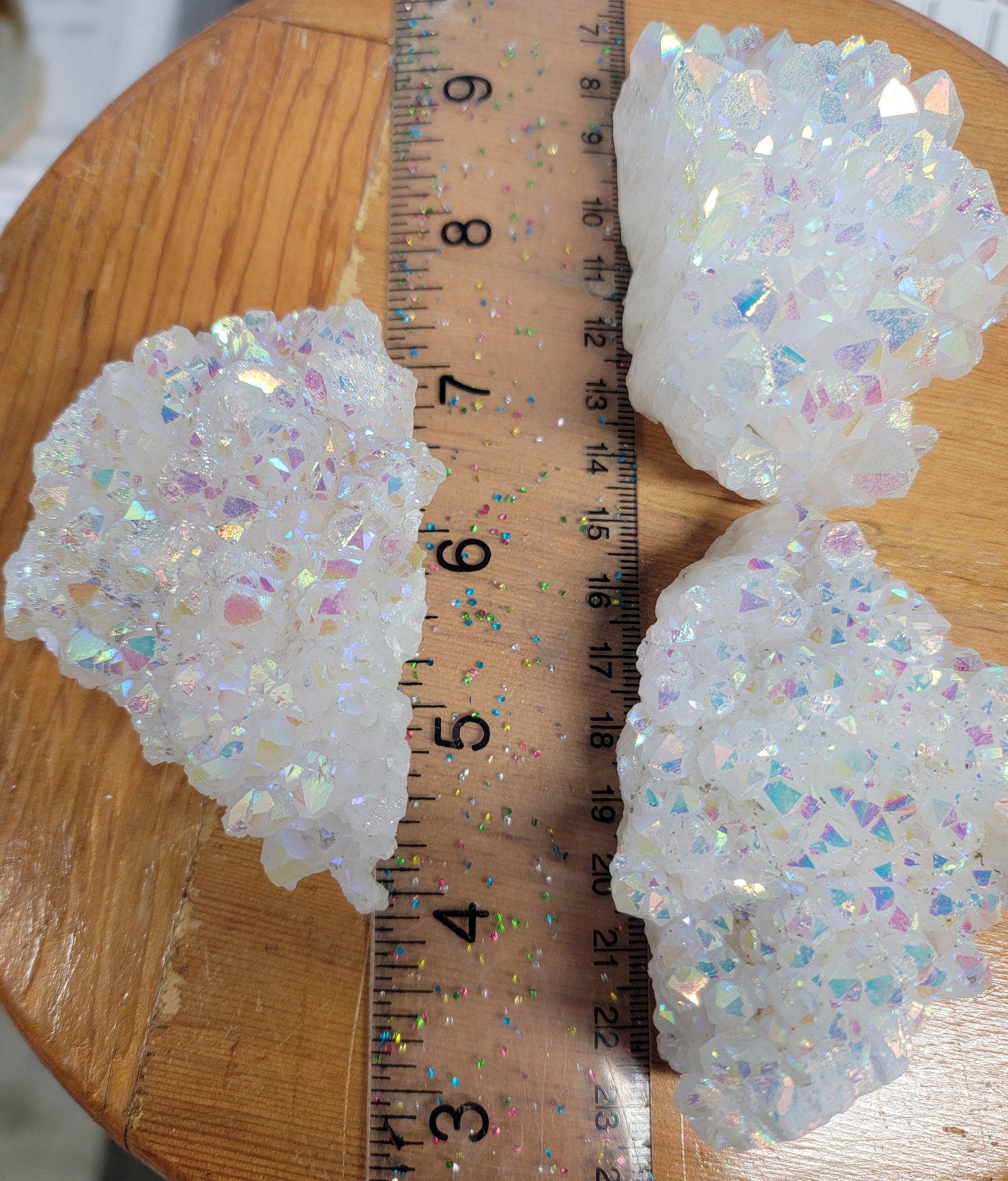 3 mesmerizing Angel Aura Quartz clusters featuring iridescent pastel hues, reflecting shades of pink, purple, and blue, with delicate crystal formations, displayed next to a ruler.  Each cluster is 3”-4” long .