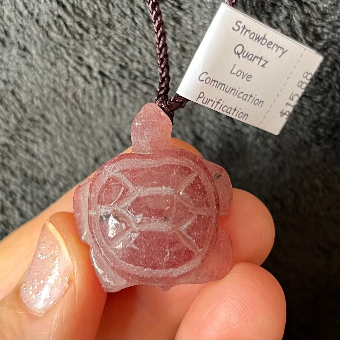 ￼close up of a turtle pendant made from strawberry quartz, suspended from an adjustable brown cord.  "Strawberry quartz is a beautiful, translucent pink quartz crystal speckled with dark red mineral inclusions." 