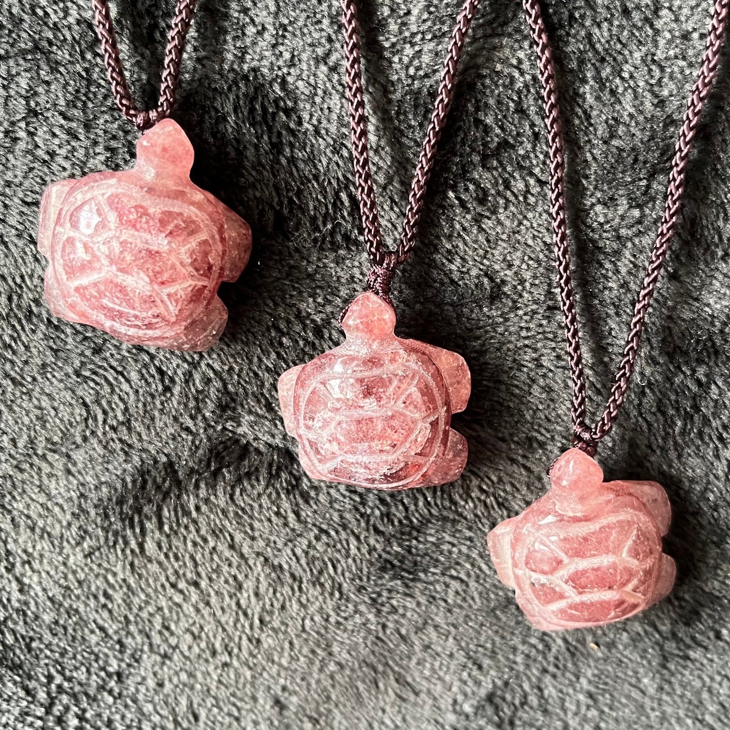 Three strawberry quartz turtle pendants, suspended from adjustable brown cords