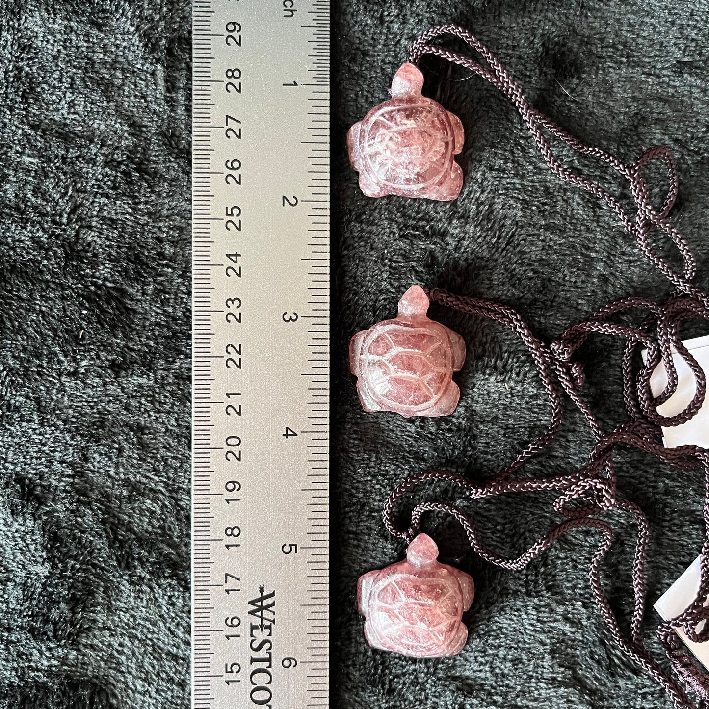 Three strawberry quartz turtle pendants displayed next to a ruler to show size. Pendants are approximately 1 inch long.