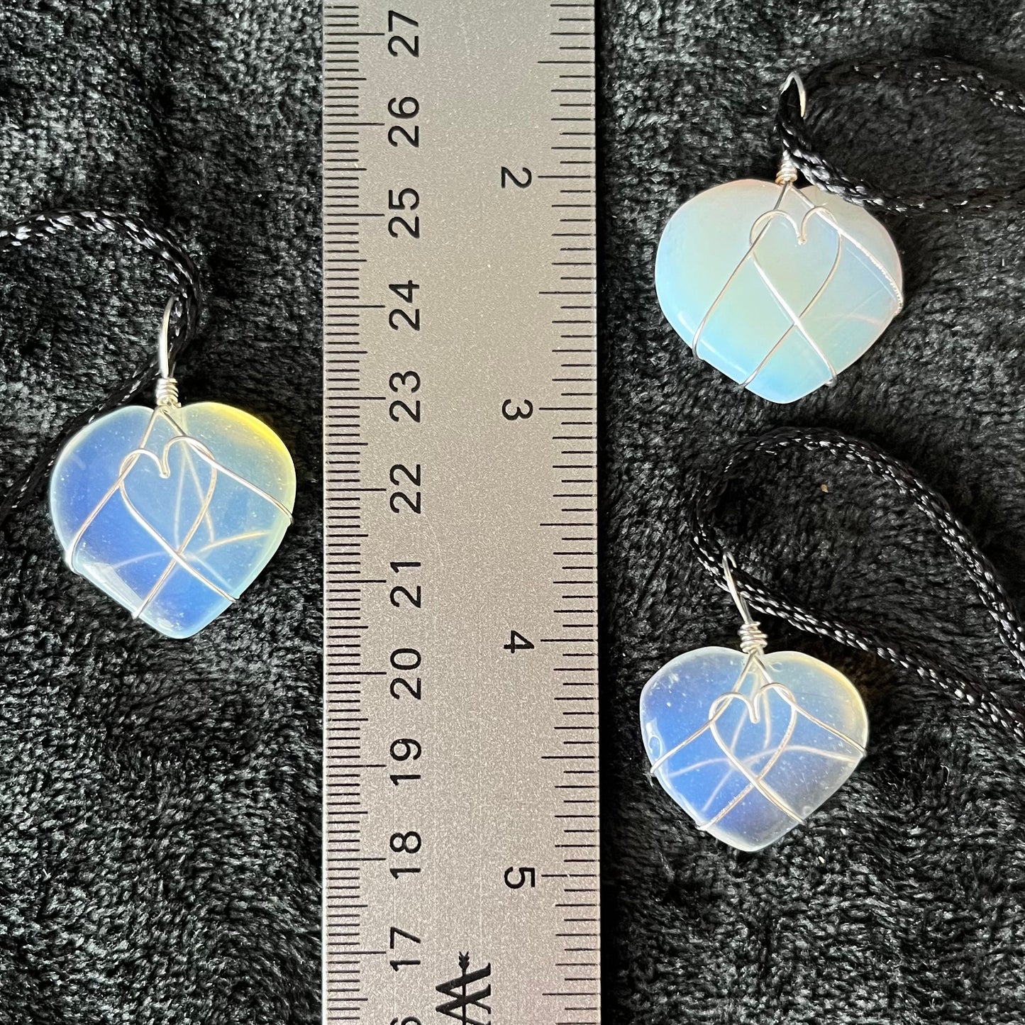 3 silver wire wrapped transluscent white opalite heart pendants, approximately 1" long, attatched to black cords, displayed next to a ruler