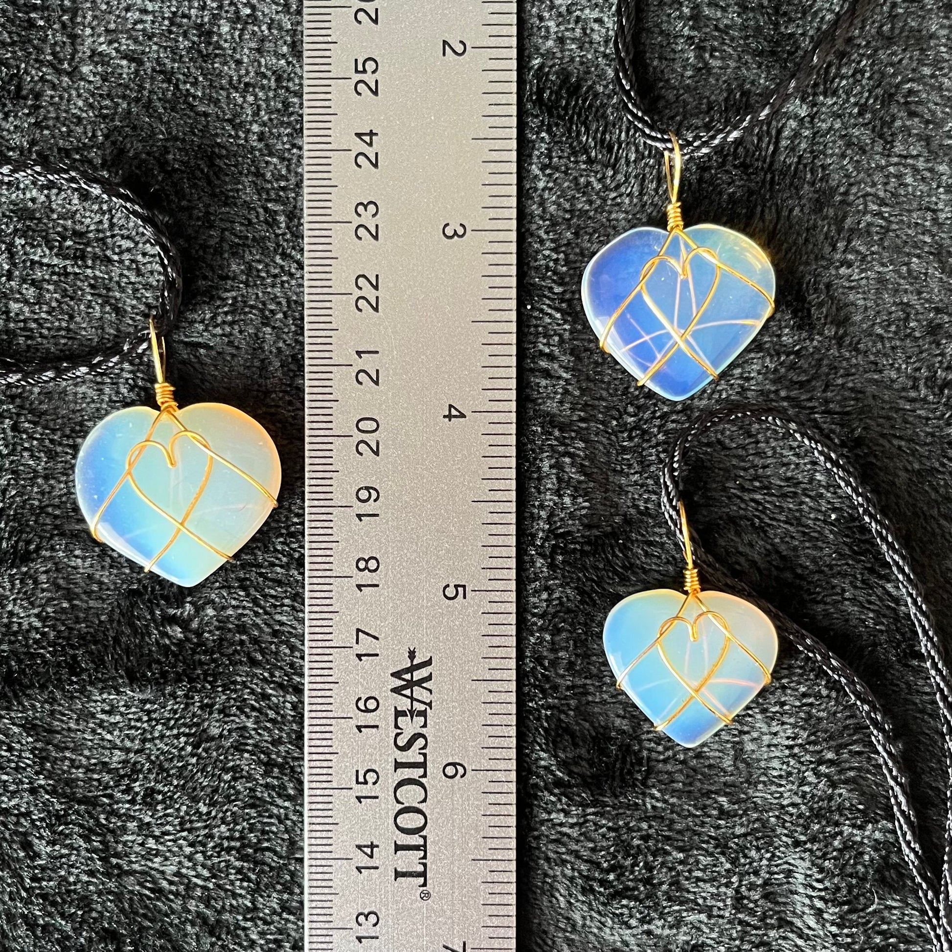 3 gold wire wrapped transluscent white opalite heart pendants, approximately 1" long, attatched at a black cords, displayed next to a ruler.