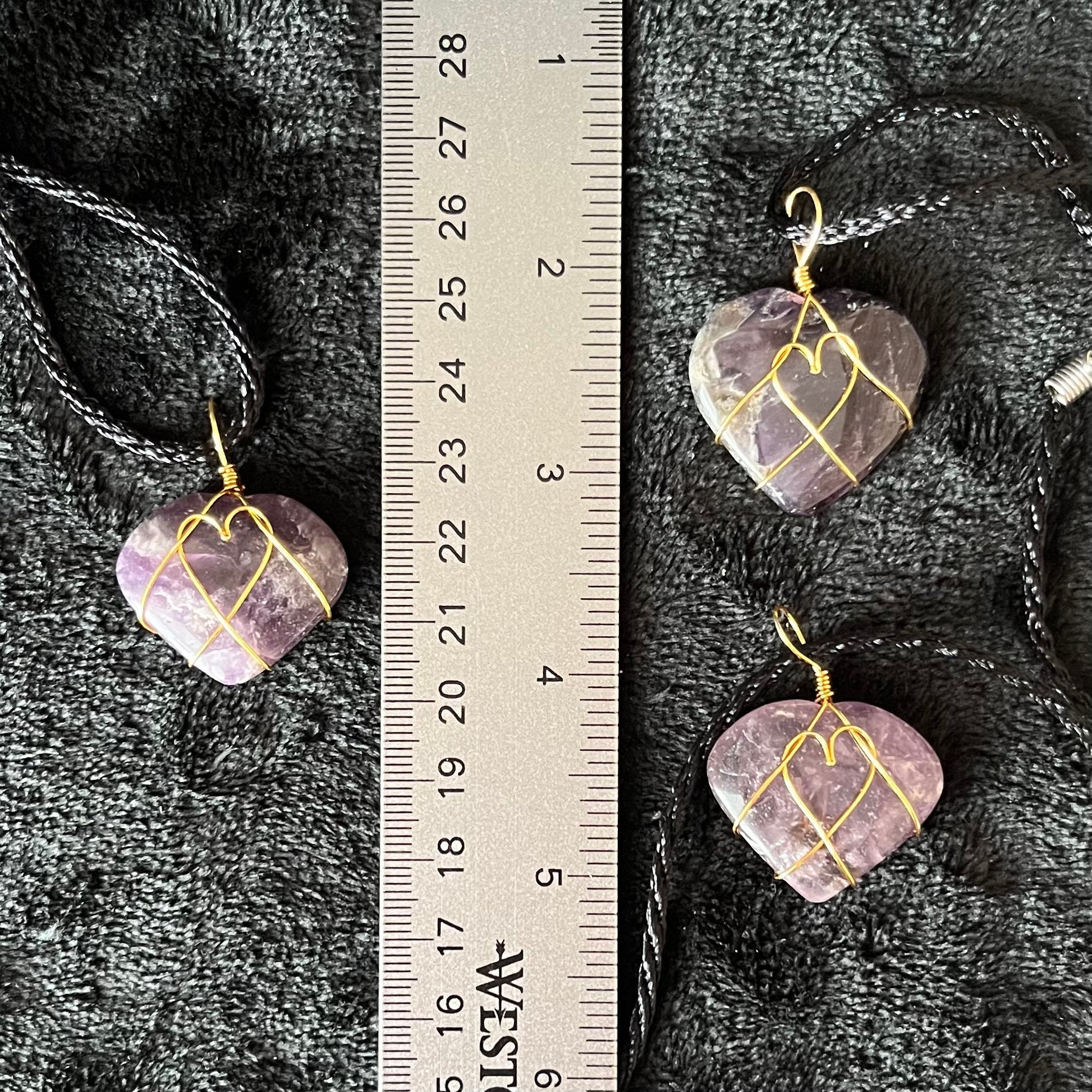 close up of 1 inch purple and white amethyst heart, gold wire wrapped pnedant attached to a black cord, displayed next to a ruler.