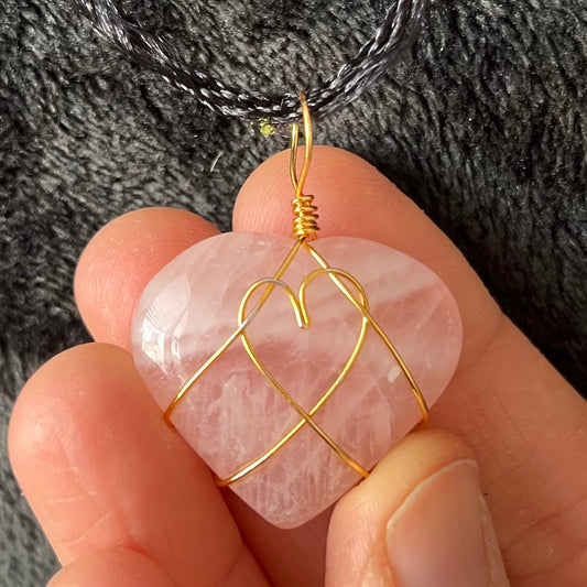 Wire-wrapped rose quartz heart necklace: a gold wire intricately wraps around a polished rose quartz heart pendant, hanging on a delicate chain.  The wire makes a heart shape in the middle of the rose quartz heart