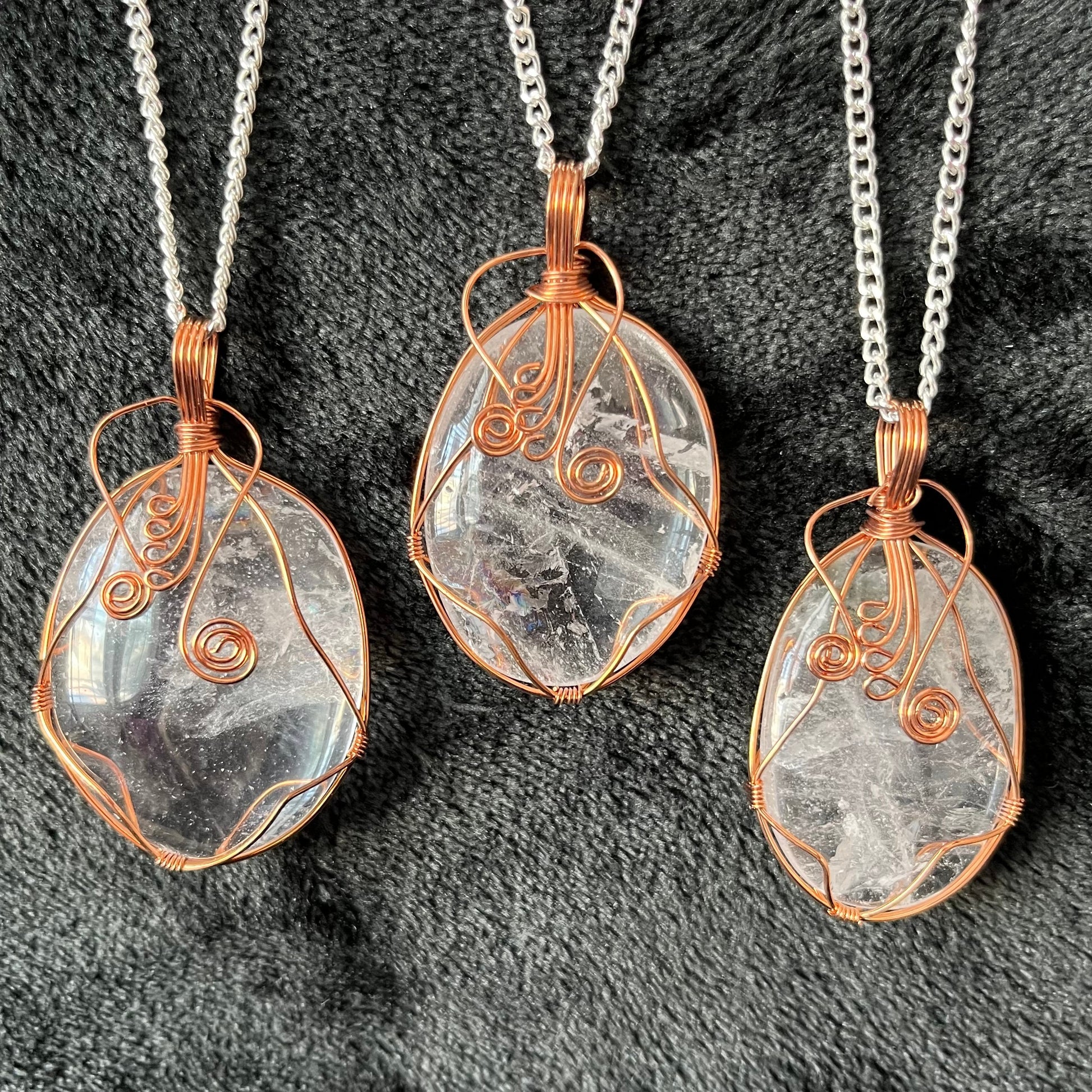 3 shiny marbled clear quartz oval pendants fancy copper wire wrapped pendants, each attached to a silver chain.