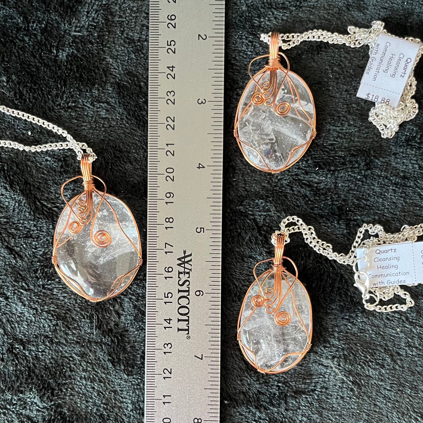 Three fancy copper wire wrapped clear quartz oval stone pendants attatched to a silver chains, displayed against a black background next to a ruler.  eaxh oendant is 1 3/4" -  2 1/4" long