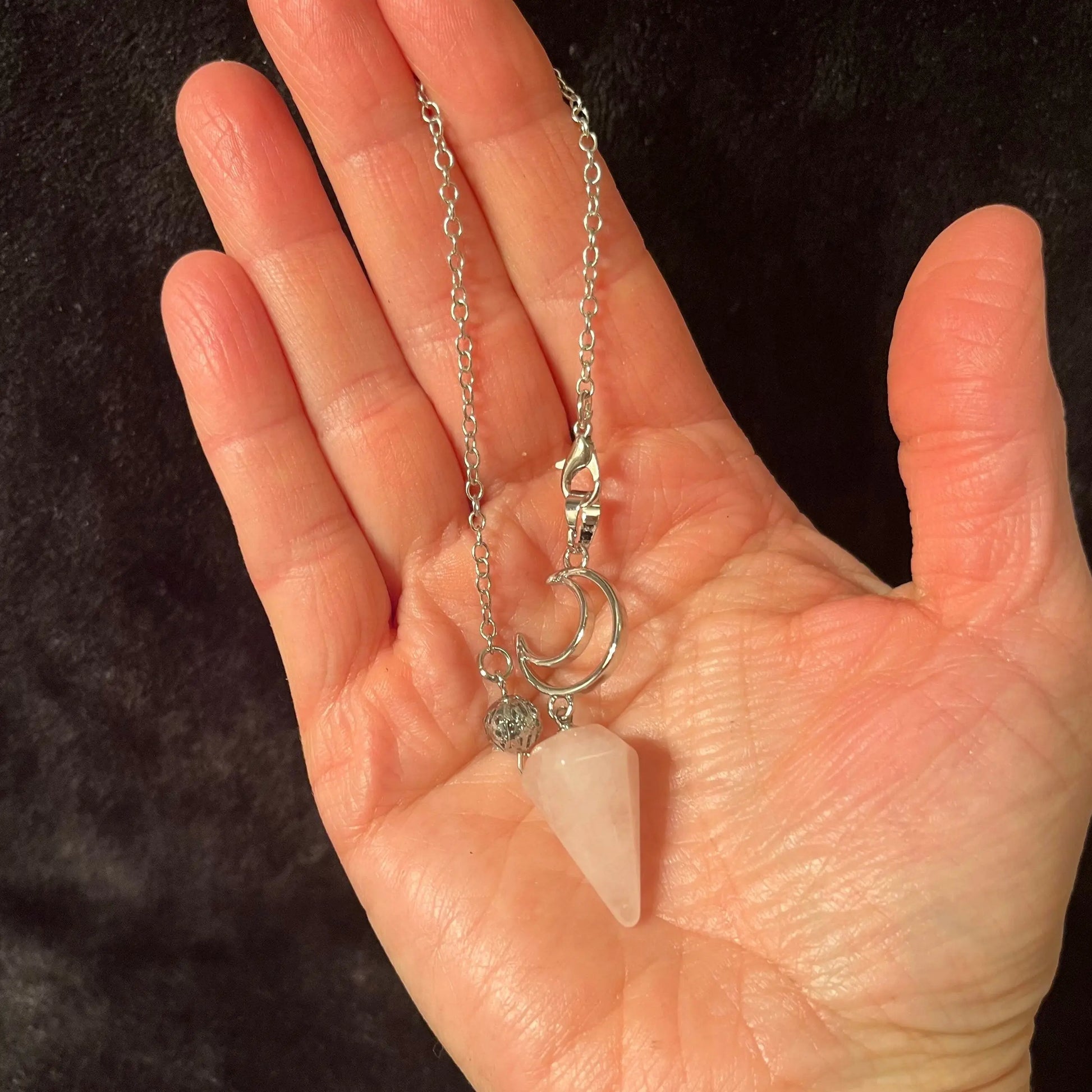 1 inch rose quartz pendulum attatched to an 8 inch silver chain including a silver crescent moon displayed delicately in the palm of a hand