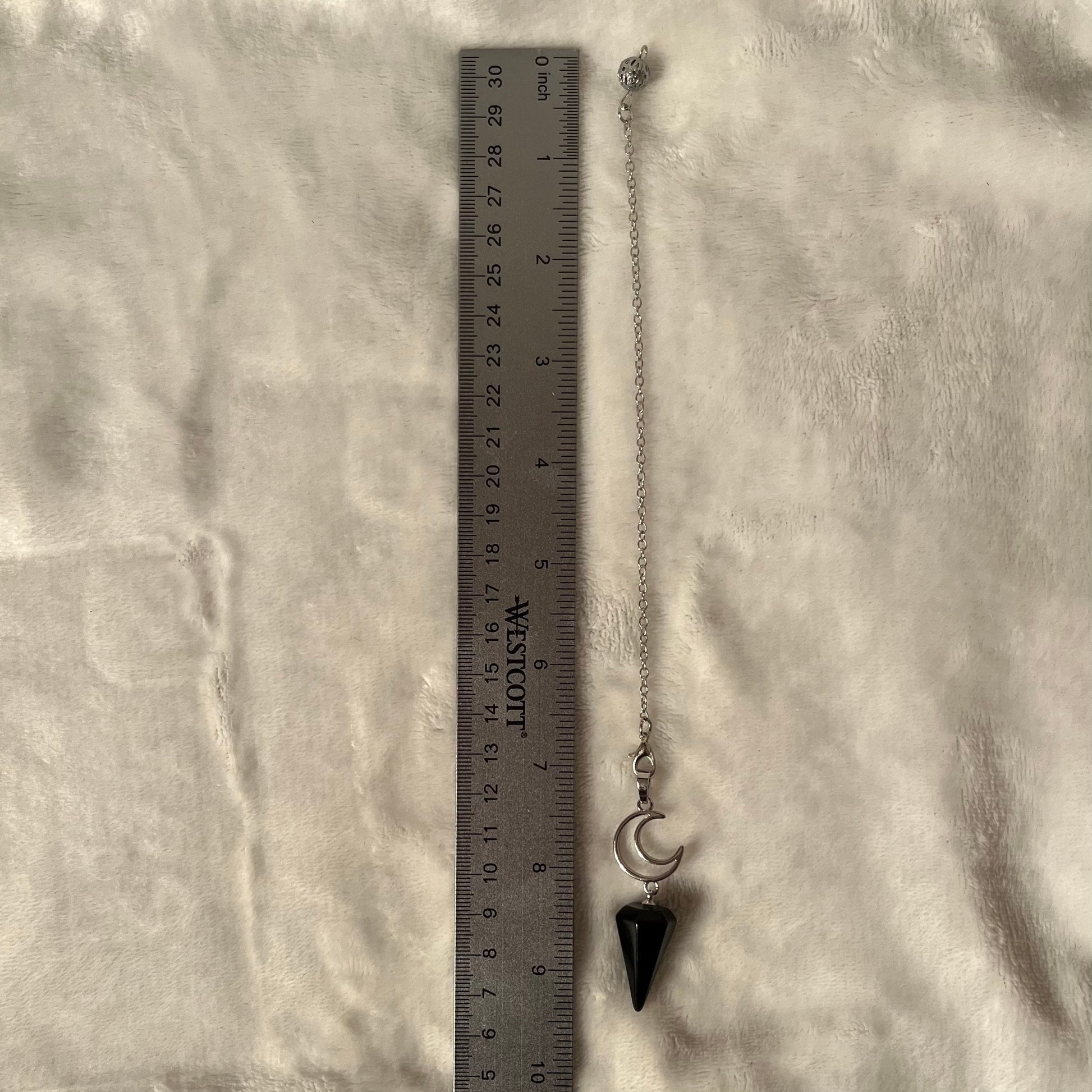 1 inch black obsidian pendulum attarched to a silver crescent moon, both connected to an 8 inch silver chain, displayed next to a silver ruler against a white background