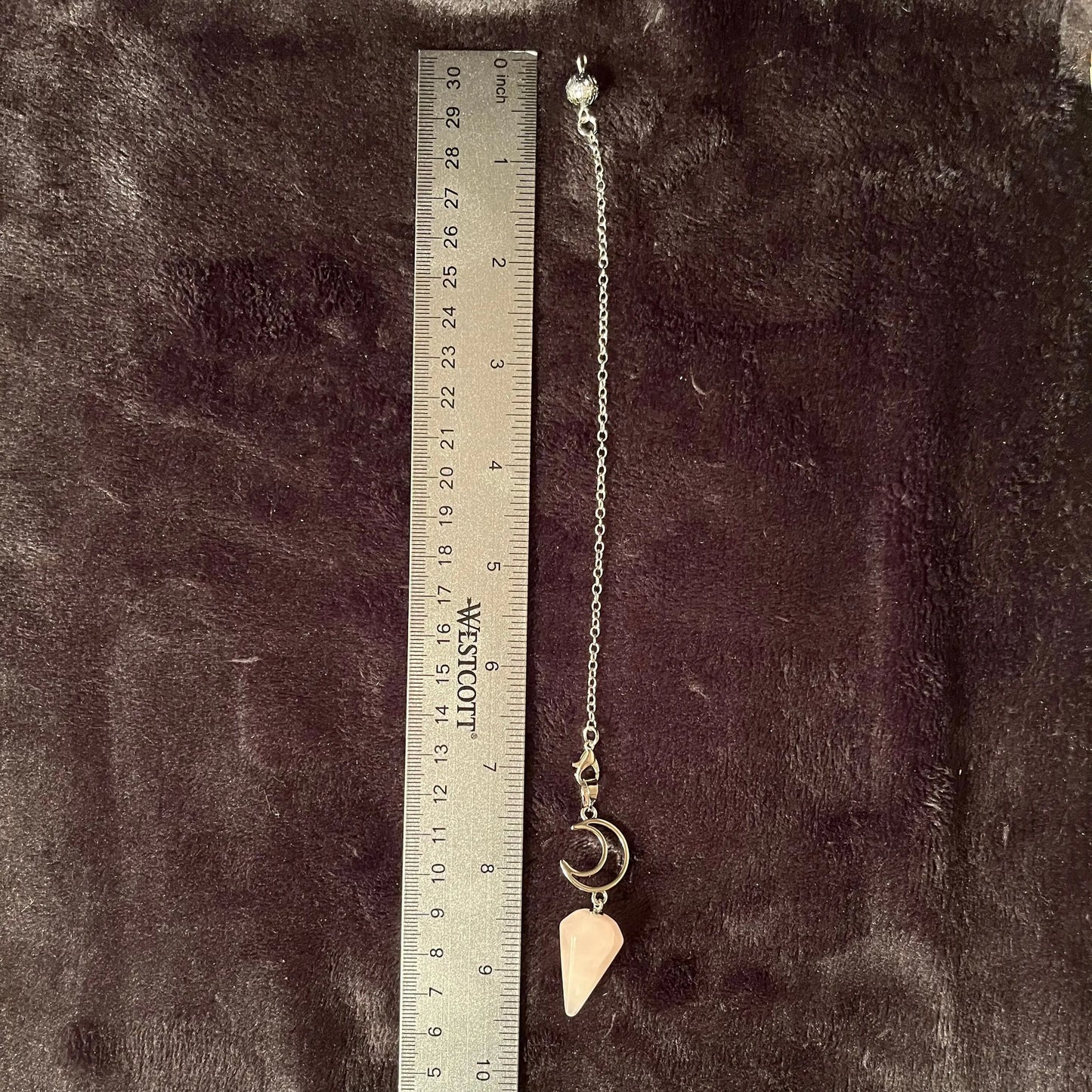 1 inch rose quartz pendulum attatched to an 8 inch silver chain including a silver crescent moon next to a ruler