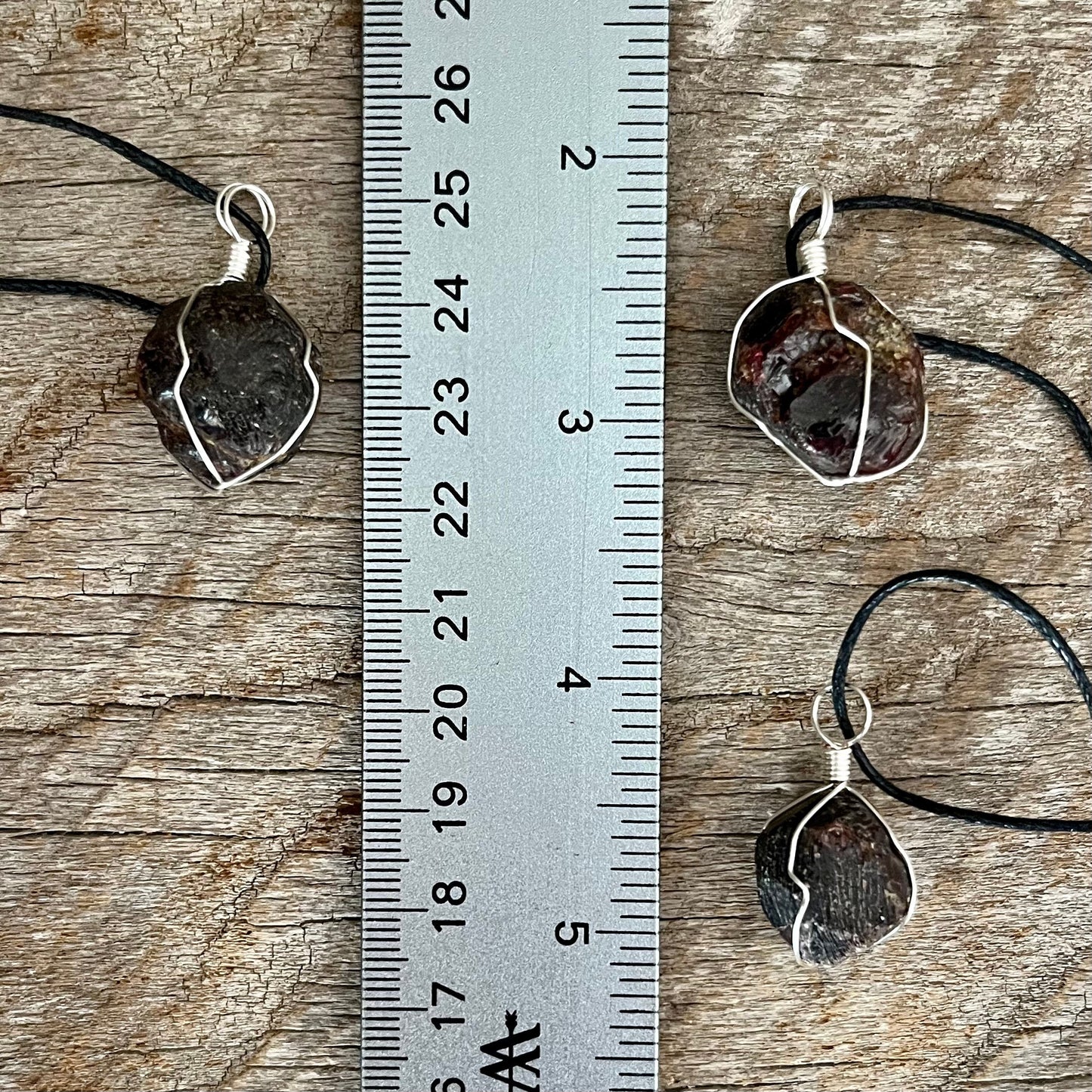 3 silver wire wrapped garnet crystal pendants attatched to adjistable black cords. displayed next to a ruler,  pendant vary in diameter from 1/2" to 3/4"